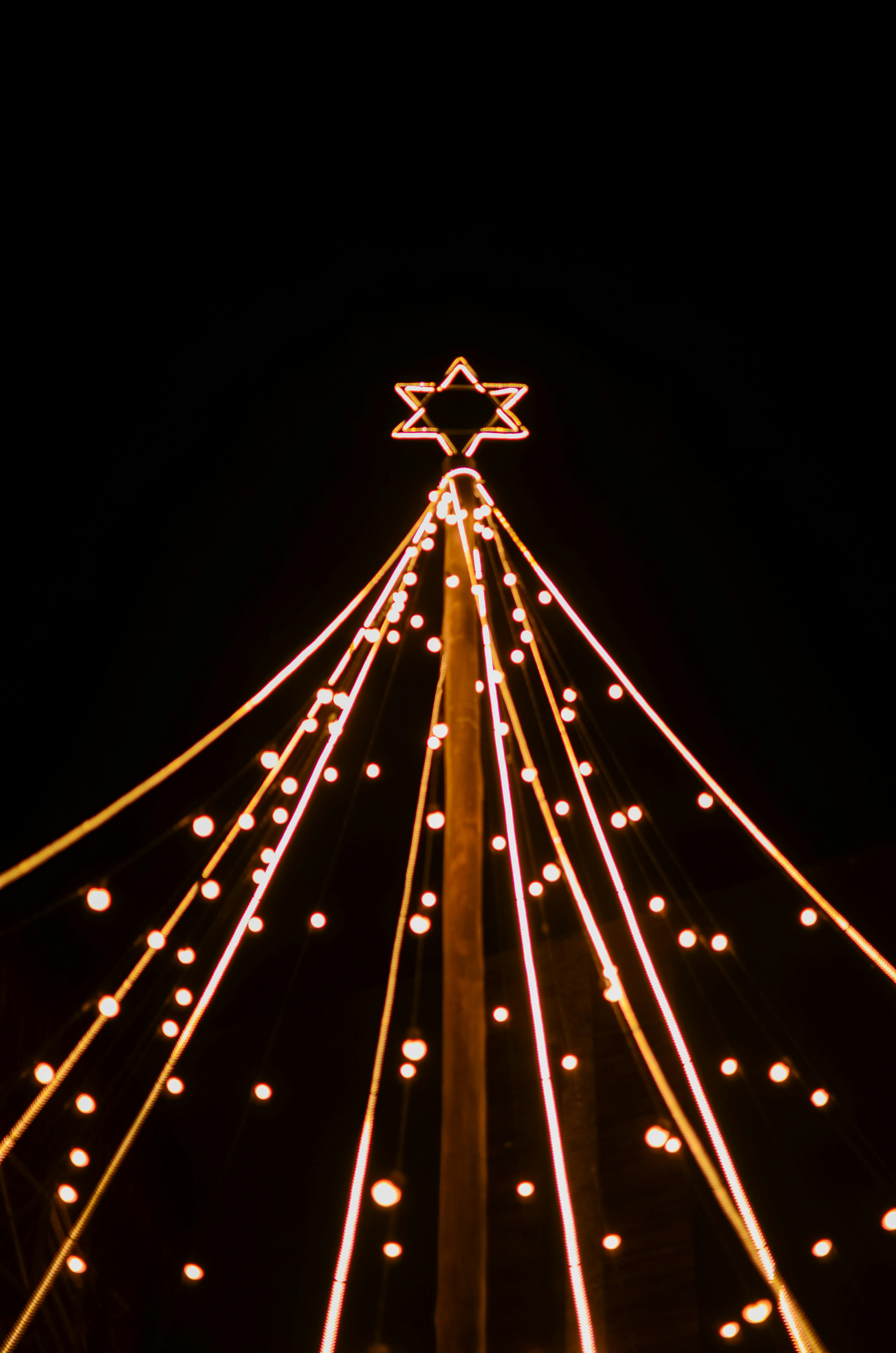 Gratuit Une étoile magnifiquement illuminée au sommet d'une structure, illuminée par des guirlandes lumineuses dans le ciel nocturne. Photos