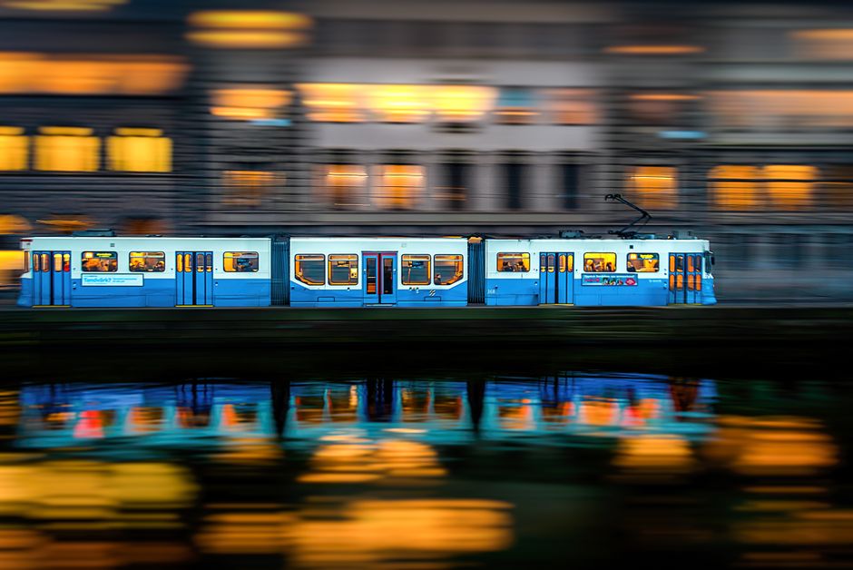 Blurred evening view of a blue tram moving through Västra Götalands län, Sweden, with reflections.
