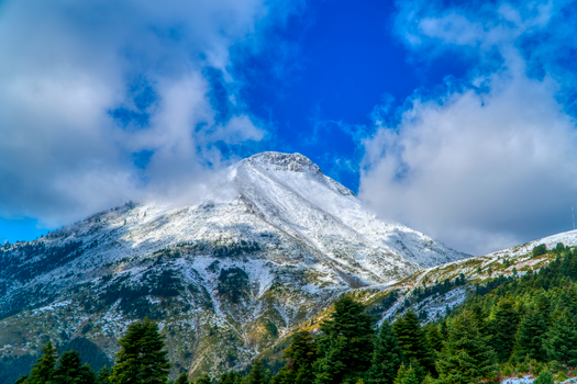 Majestic snow-covered mountain peak against a vivid blue sky in Greece.