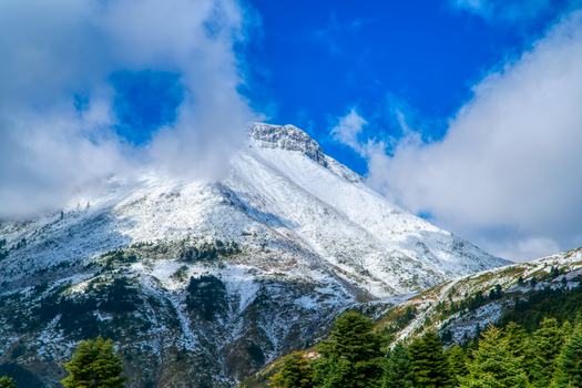 A breathtaking view of a snow-capped mountain under a clear blue sky in Greece.
