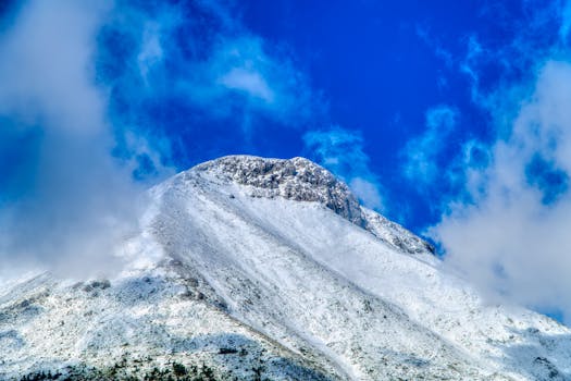 Breathtaking view of a snow-covered mountain peak in Greece with a vibrant blue sky background.