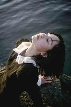 水边，一位穿着黑色连衣裙的女子闭着眼睛沉思，被画成了一幅优雅的肖像