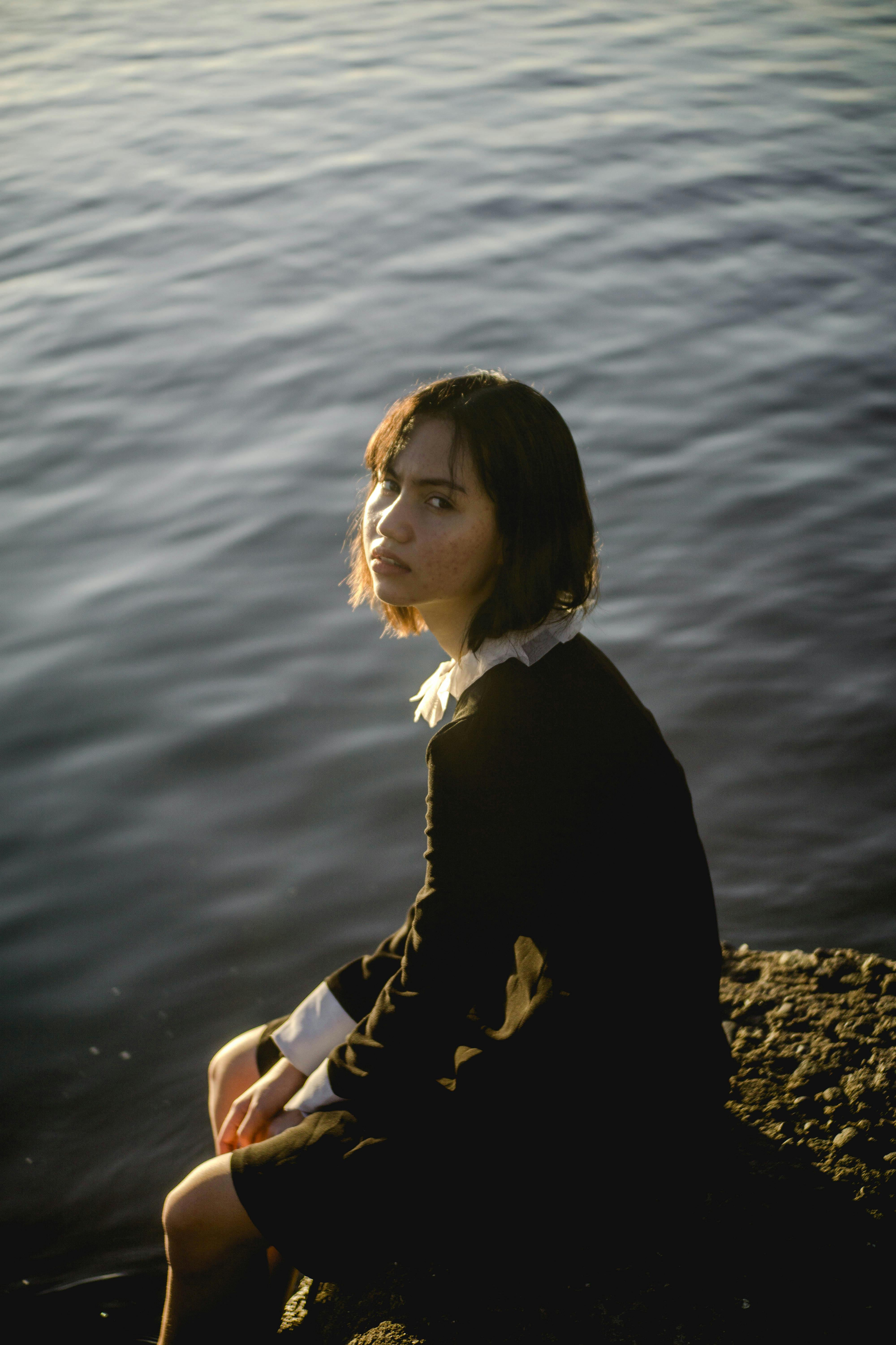 Lonely ethnic woman sitting on lake shore · Free Stock Photo