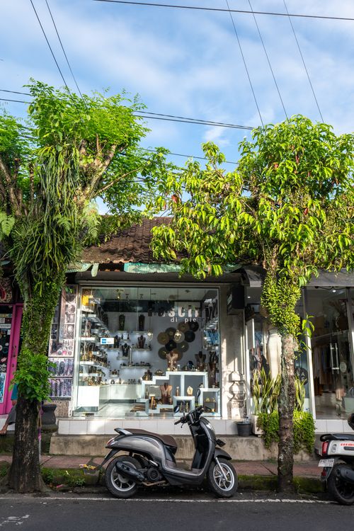 Free A scenic street in Bali featuring a parked scooter and a quaint storefront adorned with greenery. Stock Photo