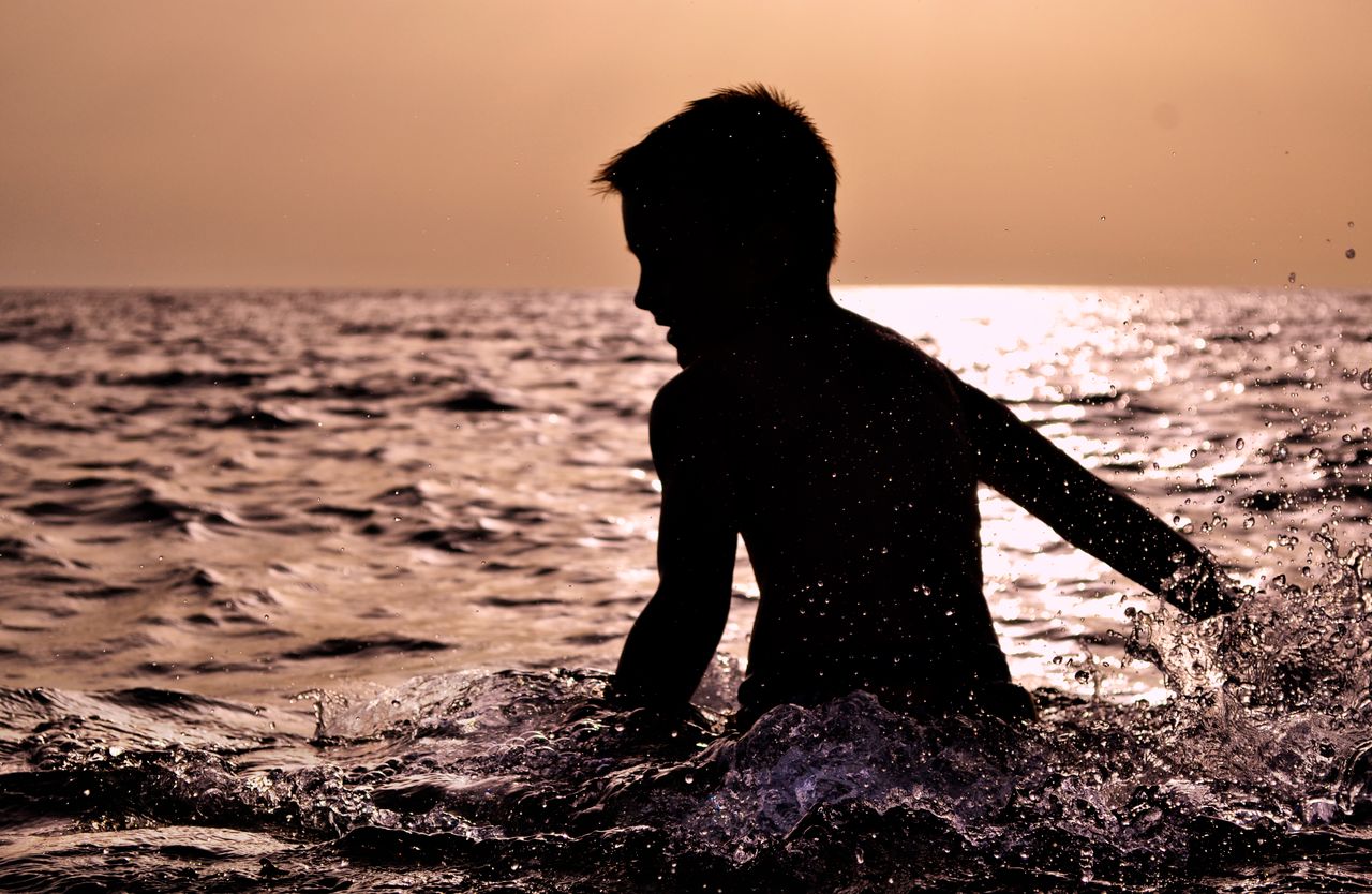 silhouette of a child splashing in the sea at sunset in zakinthos gree