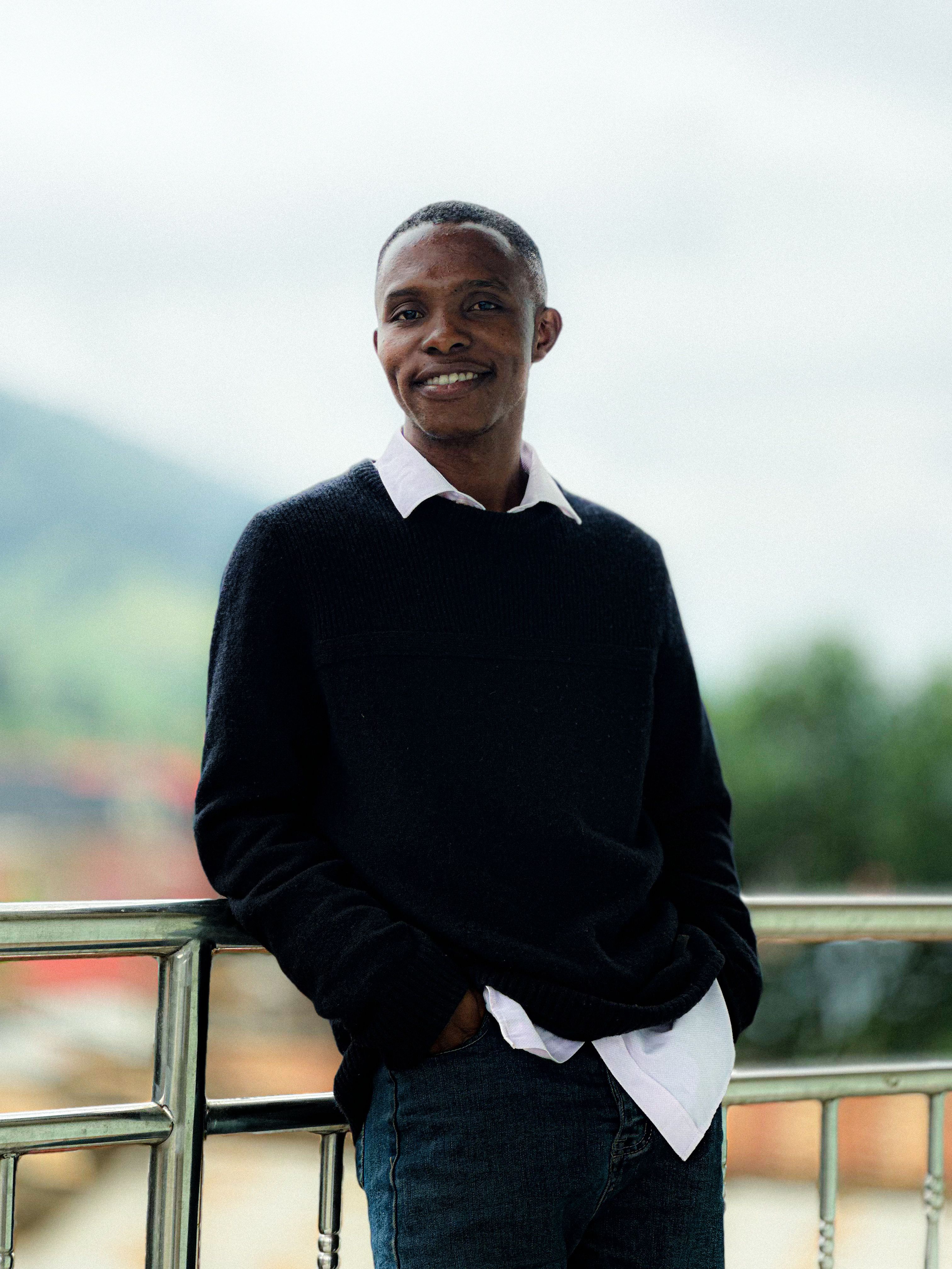 A man in casual attire smiles warmly while leaning on a railing outdoors.