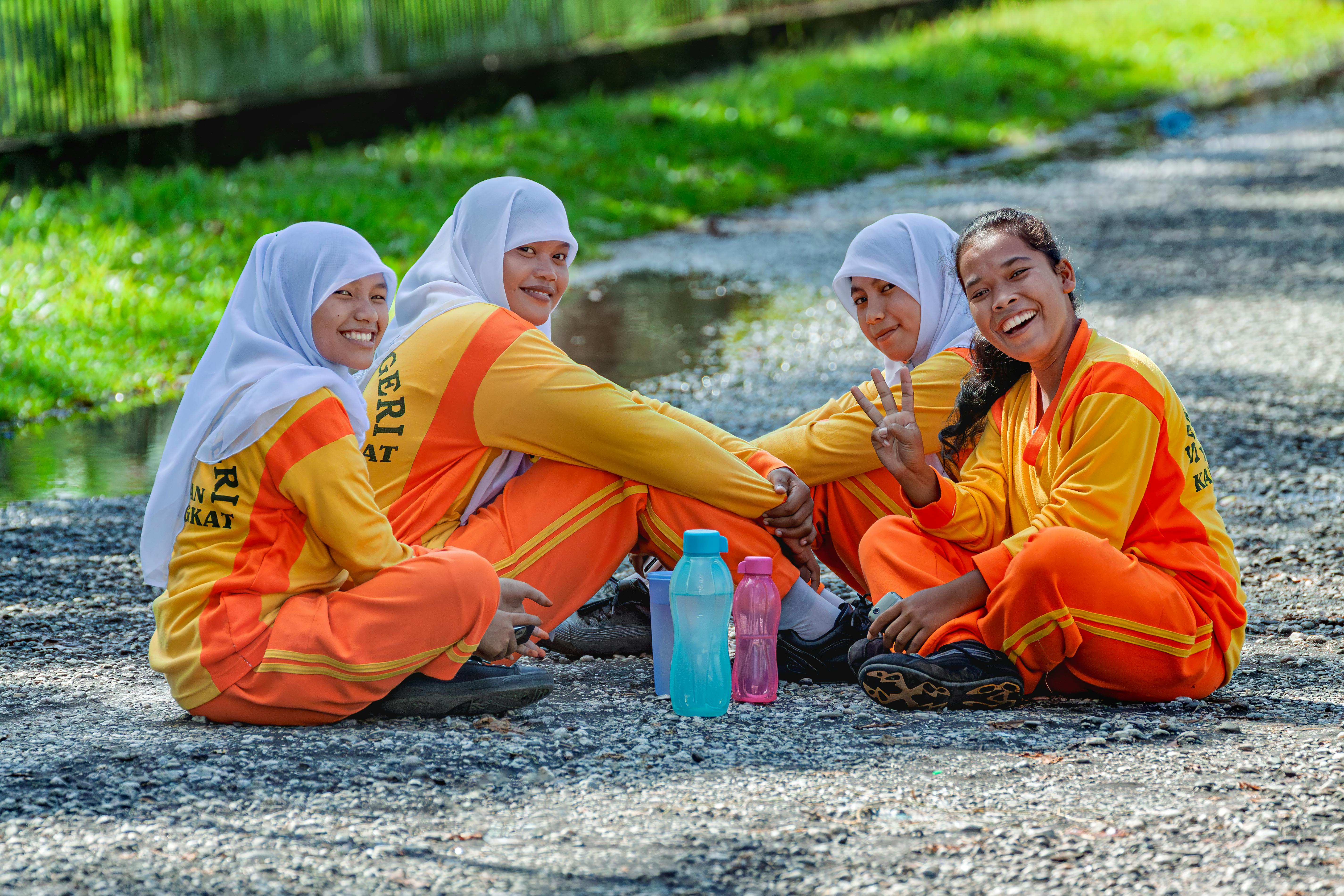 Group of Indonesian female students in traditional sportswear sitting outdoors, smiling.