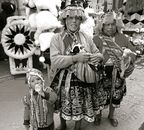 Black and white photo of an Andean family in traditional attire, holding lambs in a market setting.
