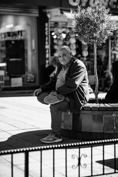 Free Black and white photo of an elderly man sitting on a bench in a city street. Stock Photo
