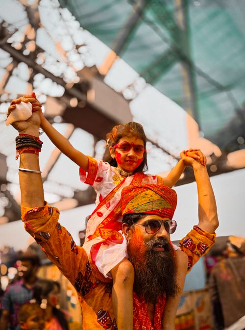 Free Father carrying daughter on shoulders during vibrant festival with colorful attire. Stock Photo