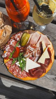 A beautiful charcuterie board with assorted meats, cheese, and drinks on a sunny outdoor wooden table.