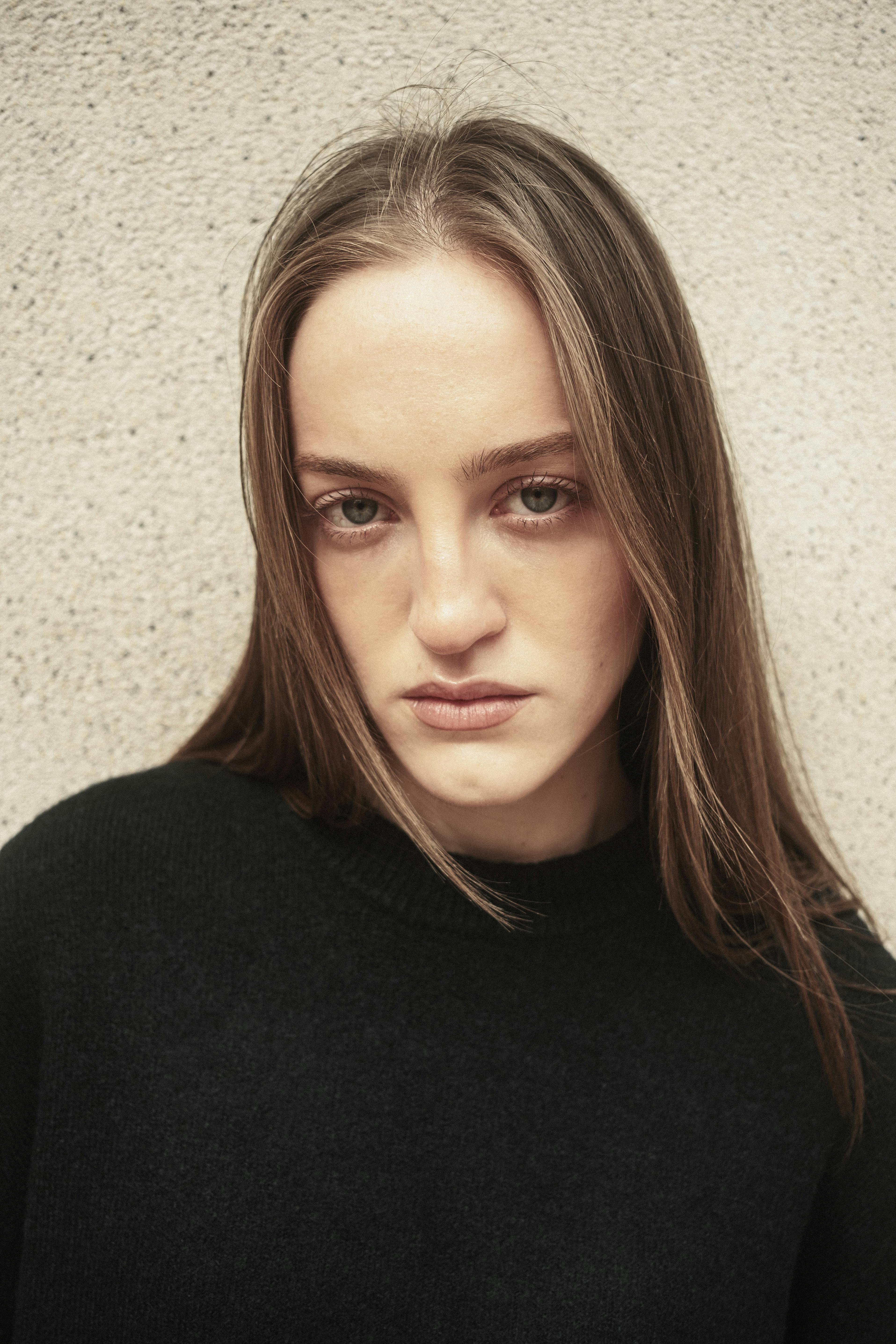 Close-up portrait of a young woman in İstanbul, Türkiye, against a textured wall.