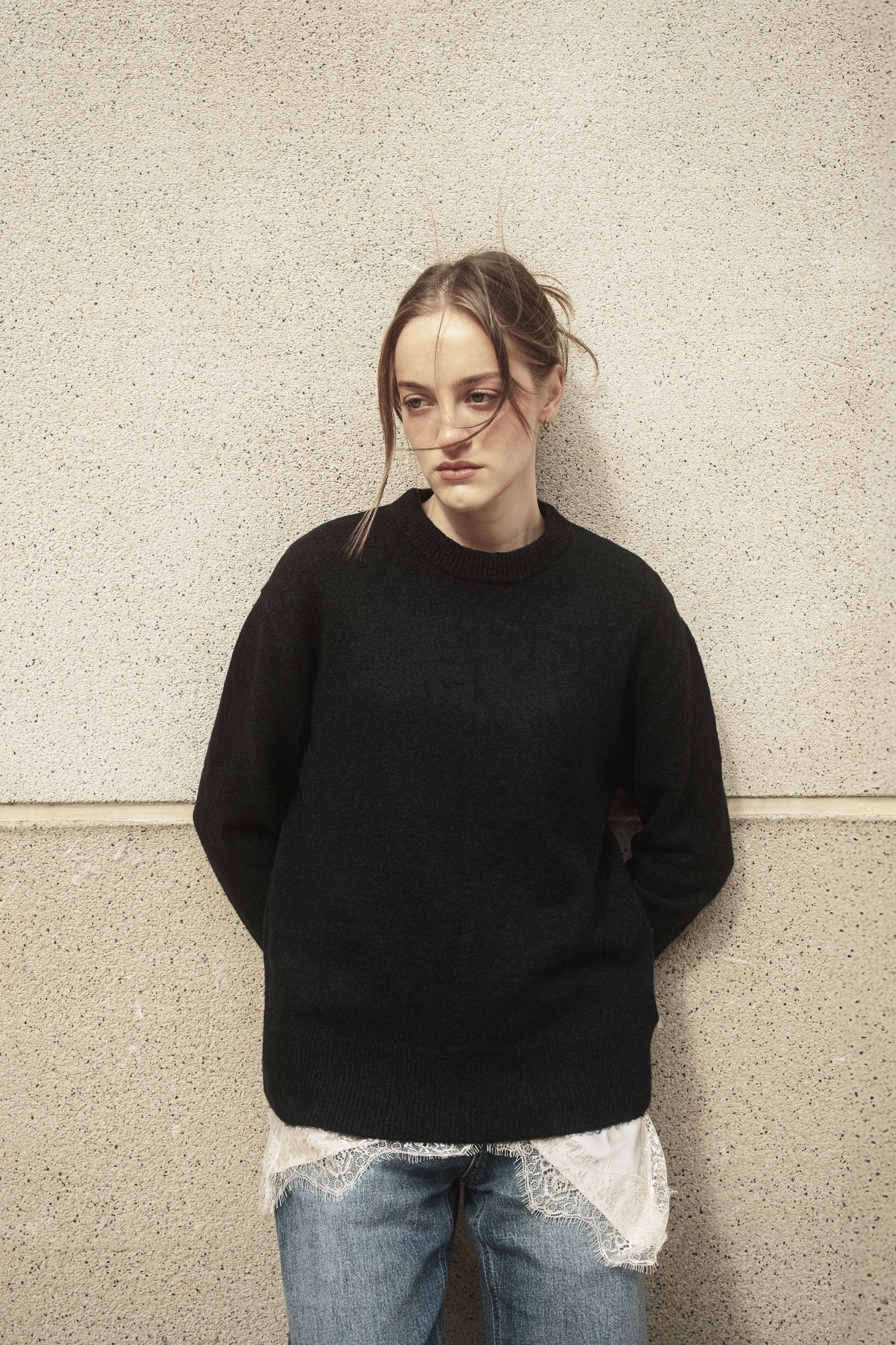 Young woman in casual attire leaning against a wall in an urban setting, İstanbul.