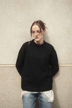 Young woman in casual attire leaning against a wall in an urban setting, İstanbul.