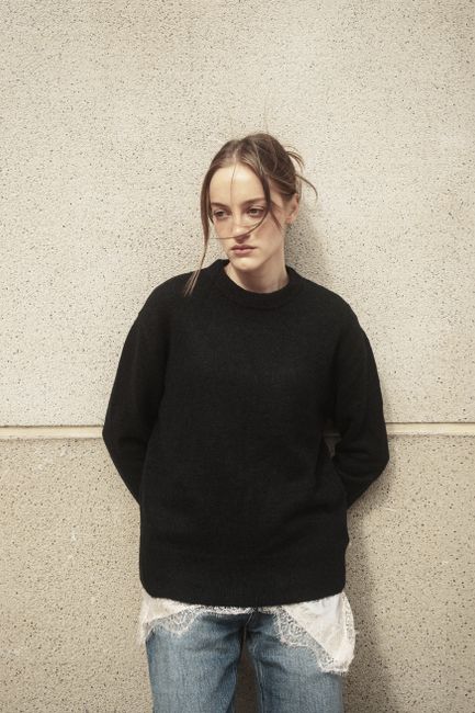 Young woman in casual attire leaning against a wall in an urban setting, İstanbul.
