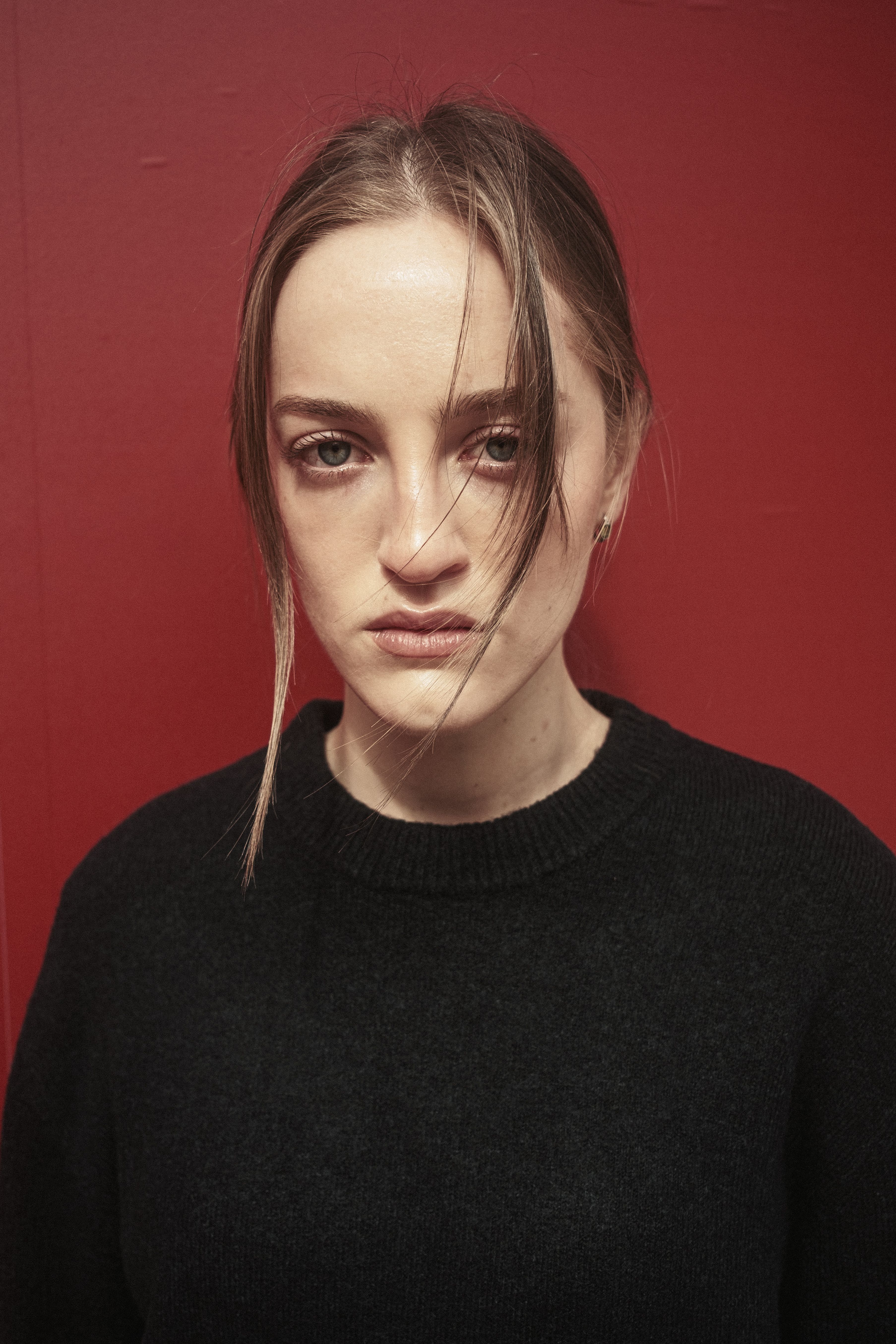Close-up portrait of a woman with a solemn expression against a vibrant red background.