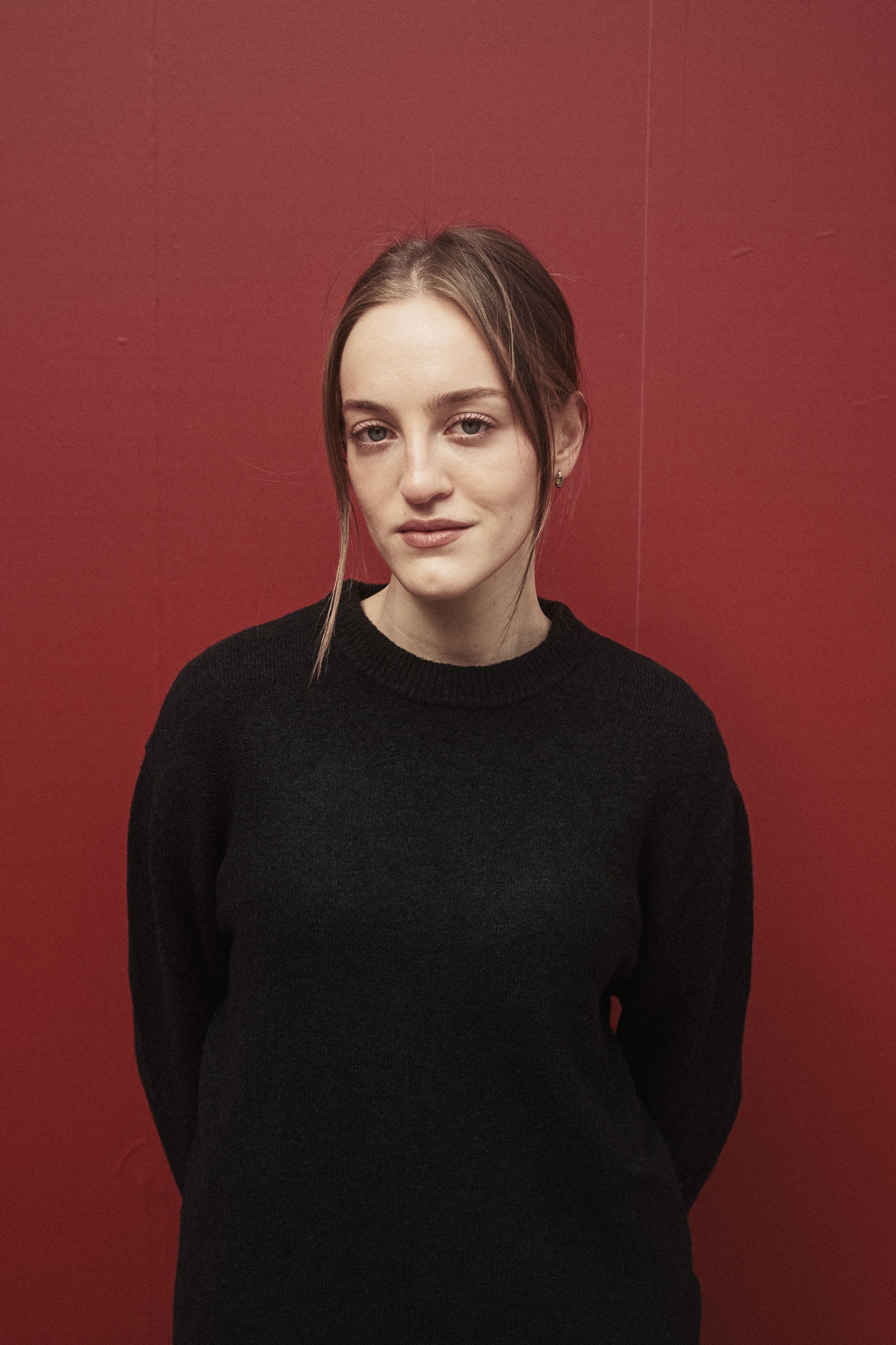 Young woman in a black sweater posing in front of a red wall in Istanbul, Turkey.