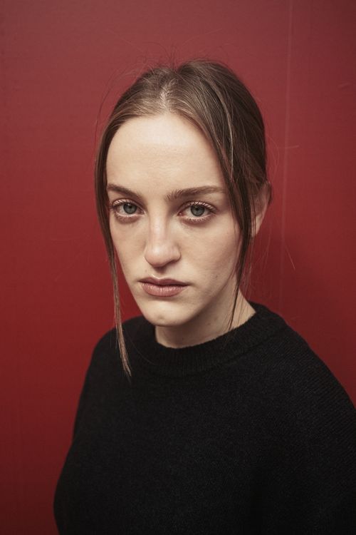 Free A serious woman stands against a red background, portraying deep thought and emotion. Stock Photo