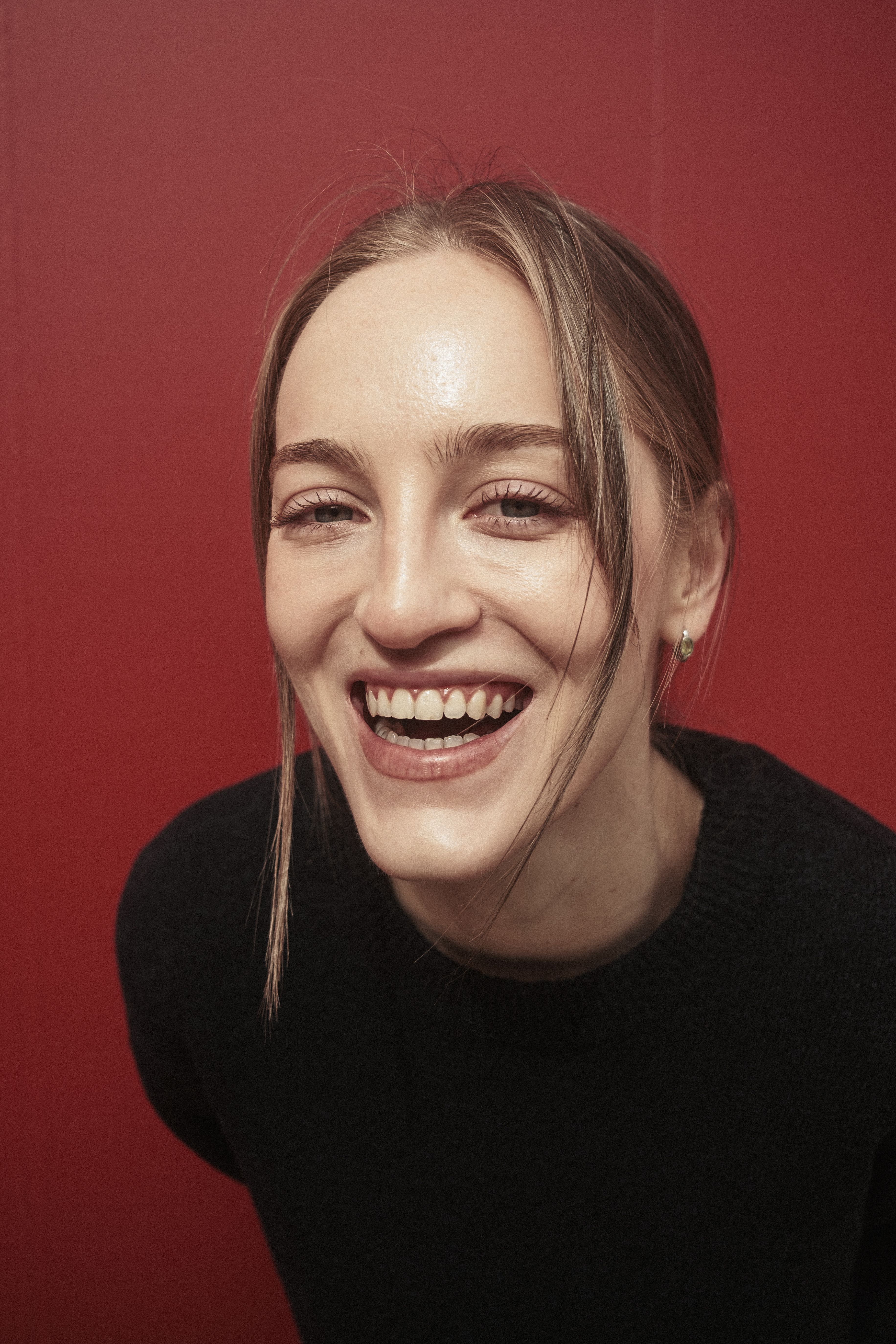 A cheerful woman smiles warmly against a vibrant red backdrop.