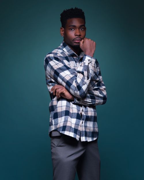 Free Elegantly posed young man in checkered shirt against teal background, exuding style and confidence. Stock Photo