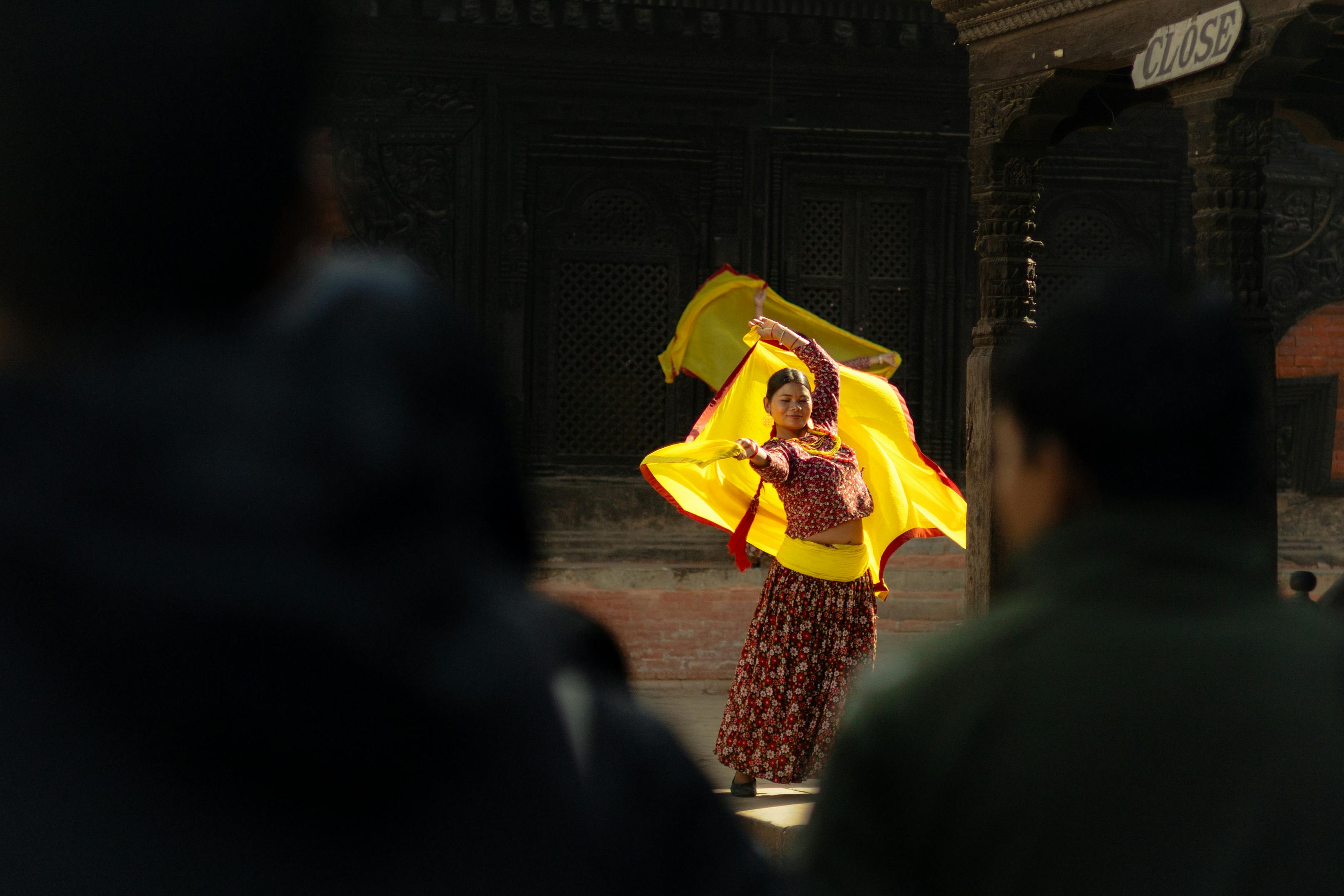 Gratis Una ballerina si esibisce in abiti tradizionali, con tessuti gialli vivaci, in un ambiente all'aperto. Foto a disposizione