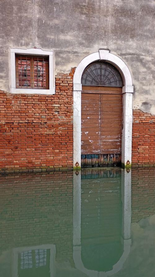 Free Charming reflection of a rustic arched doorway on a Venetian canal surface, capturing historic architecture. Stock Photo