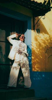 Fashionable woman in a white suit poses stylishly in a sunlit urban environment with vivid walls.