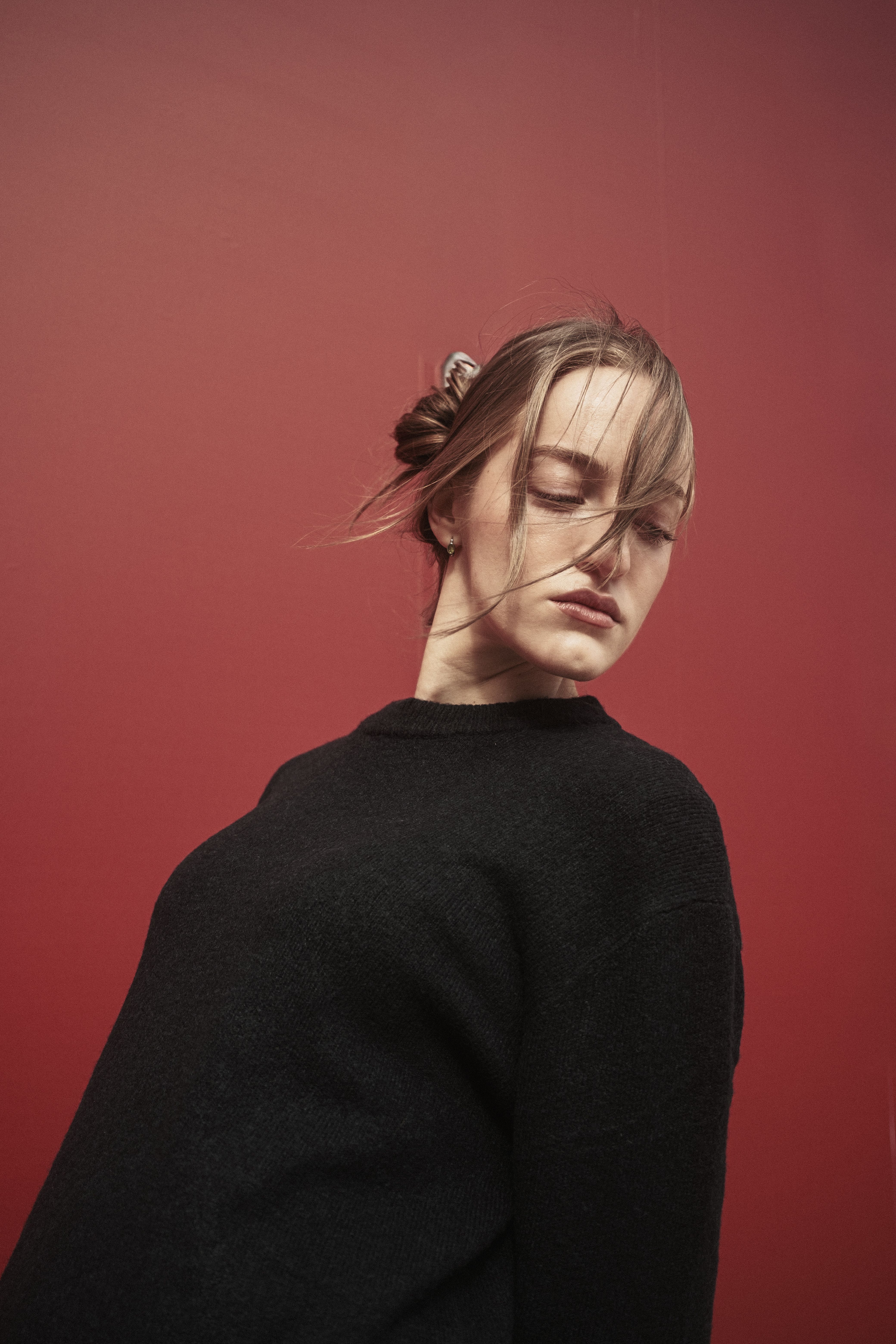 Stylish and moody portrait of a woman with windswept hair against a red backdrop.