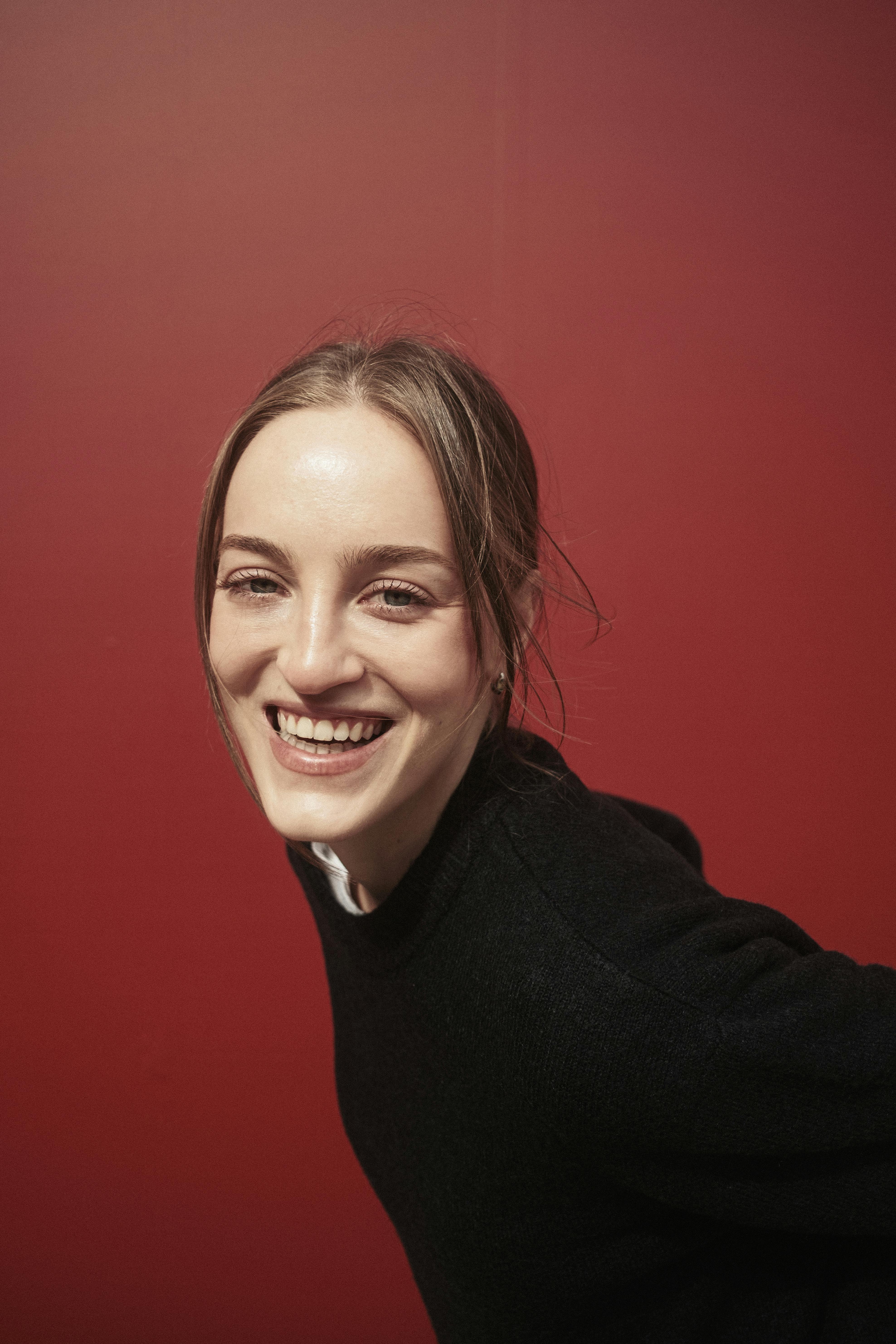 Close-up portrait of a young woman smiling against a vibrant red backdrop.