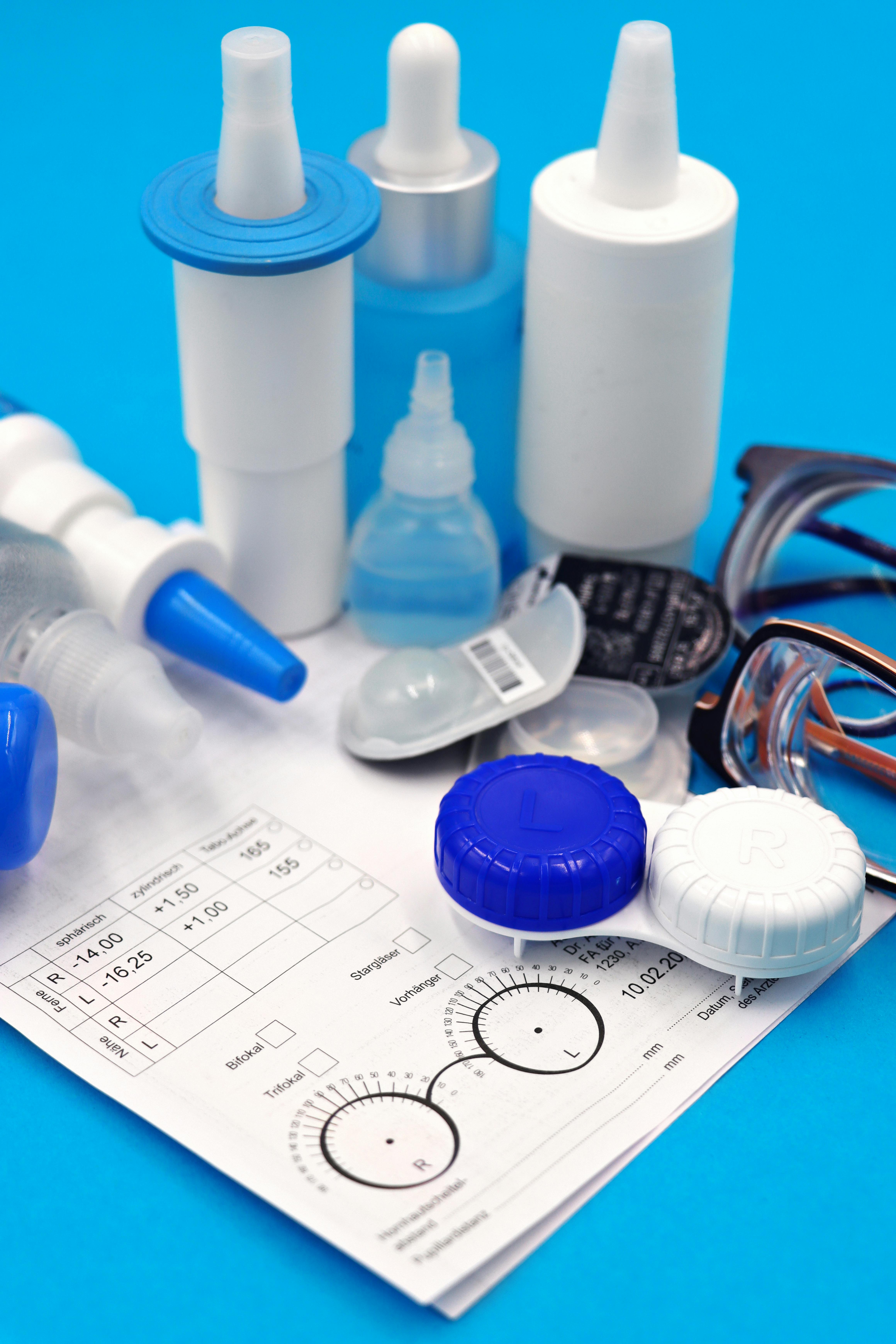 Arrangement of eye care essentials including contact lenses, eyeglasses, and solutions on blue background for vision correction.