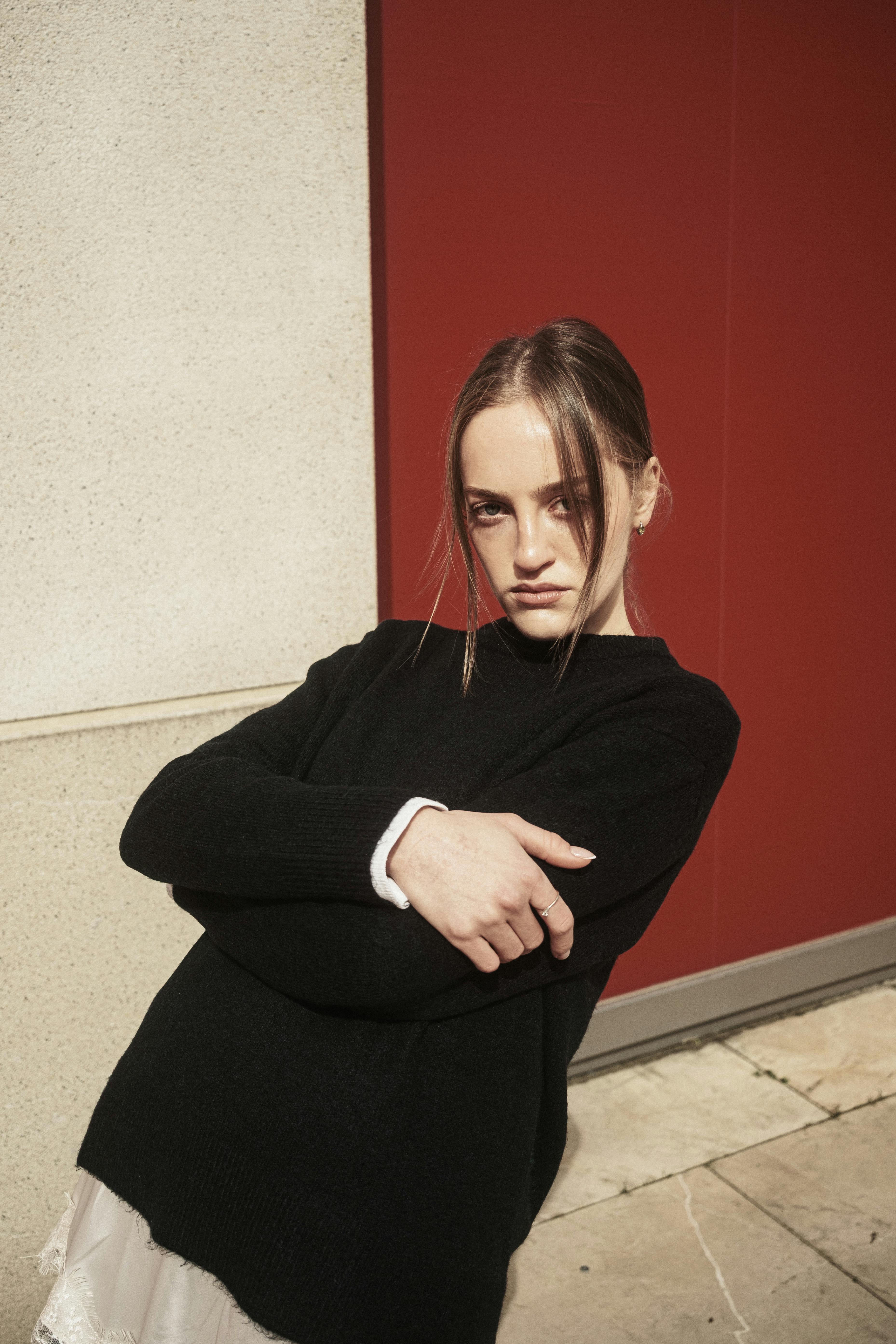 Portrait of a confident woman in dark sweater against a vibrant red wall in Istanbul, Turkey.