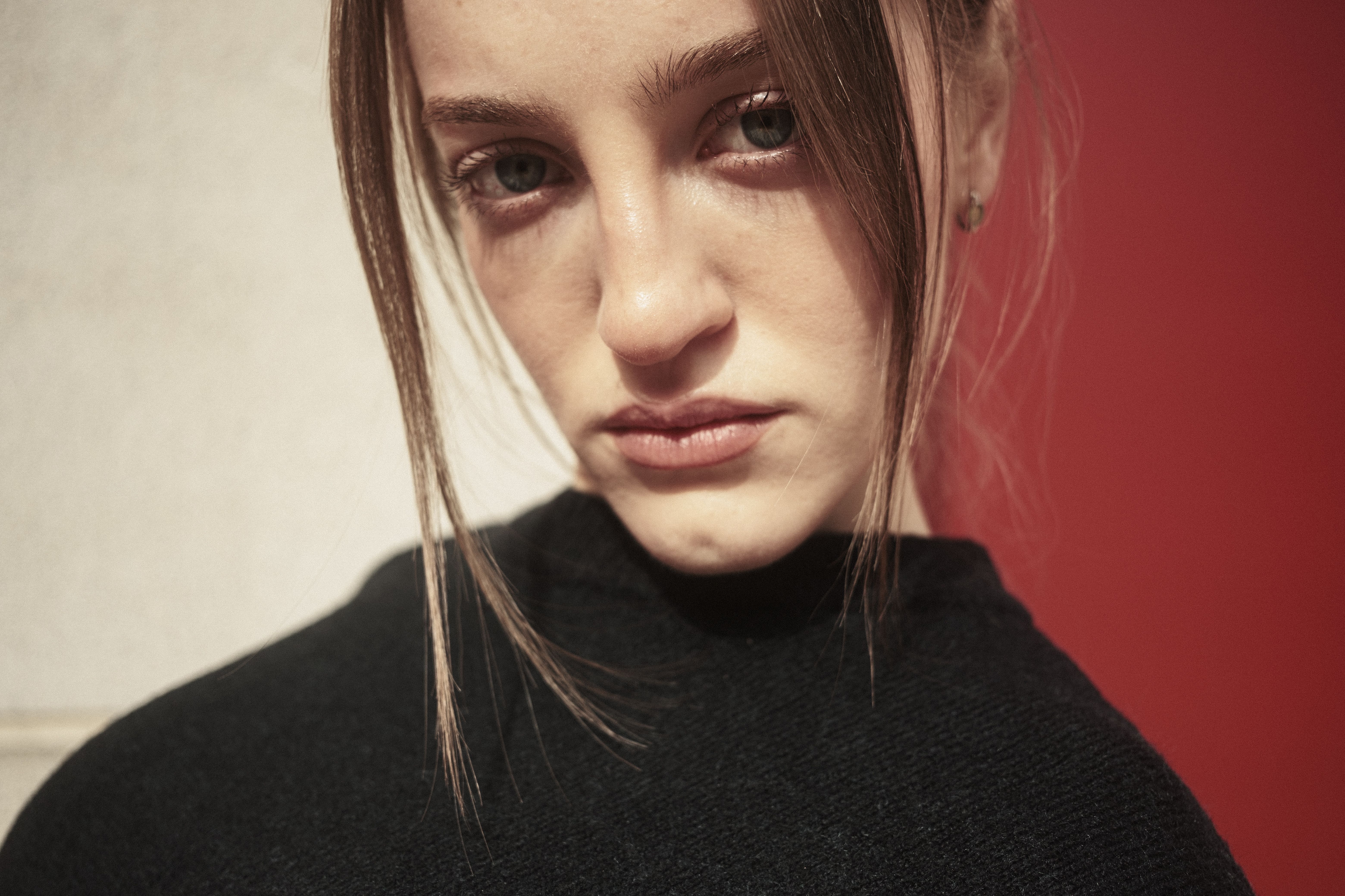 Portrait en gros plan d'une jeune femme à l'expression intense sur fond rouge et blanc.