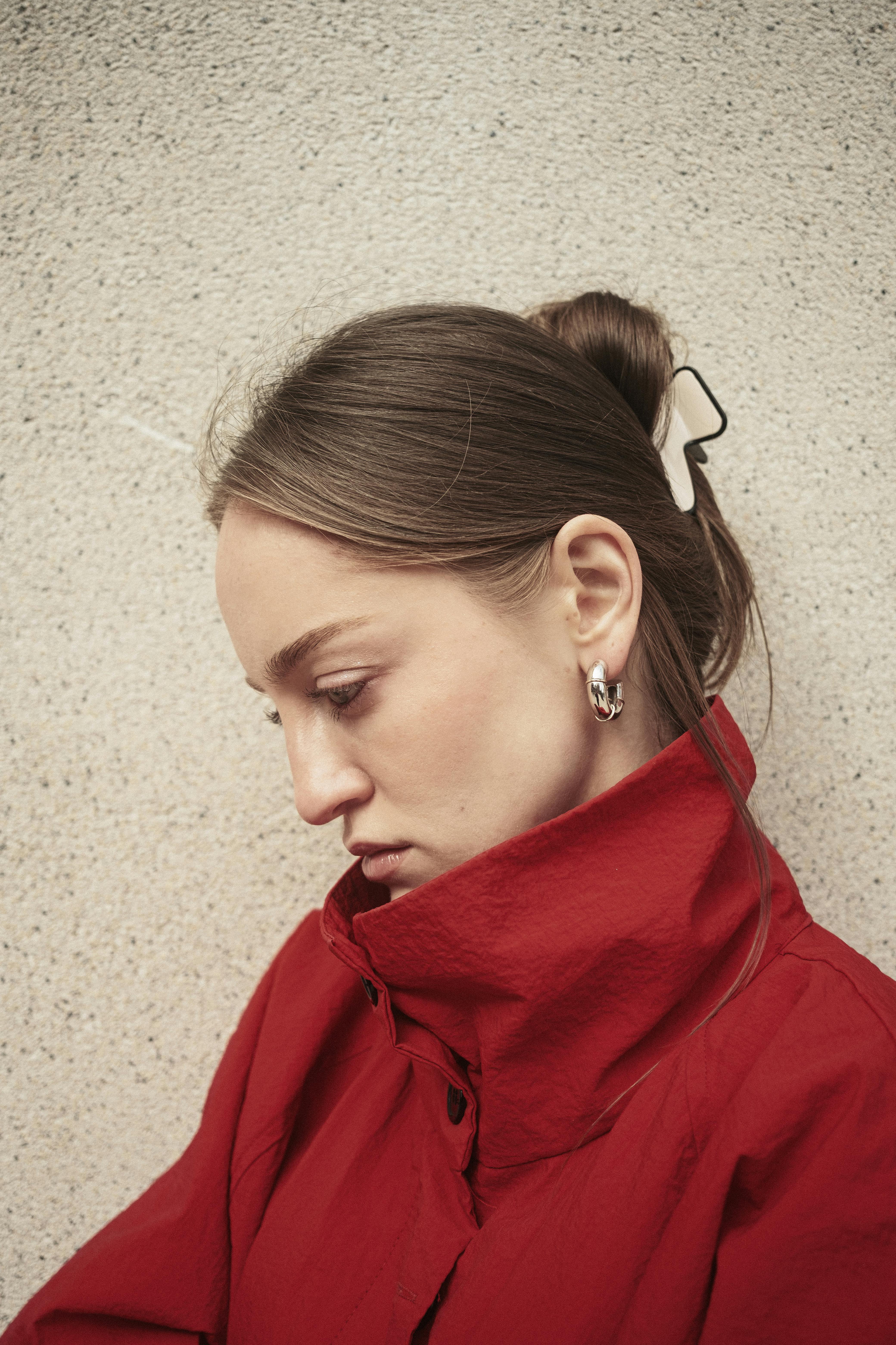 Stylish side profile of a woman in a red coat against a textured wall.