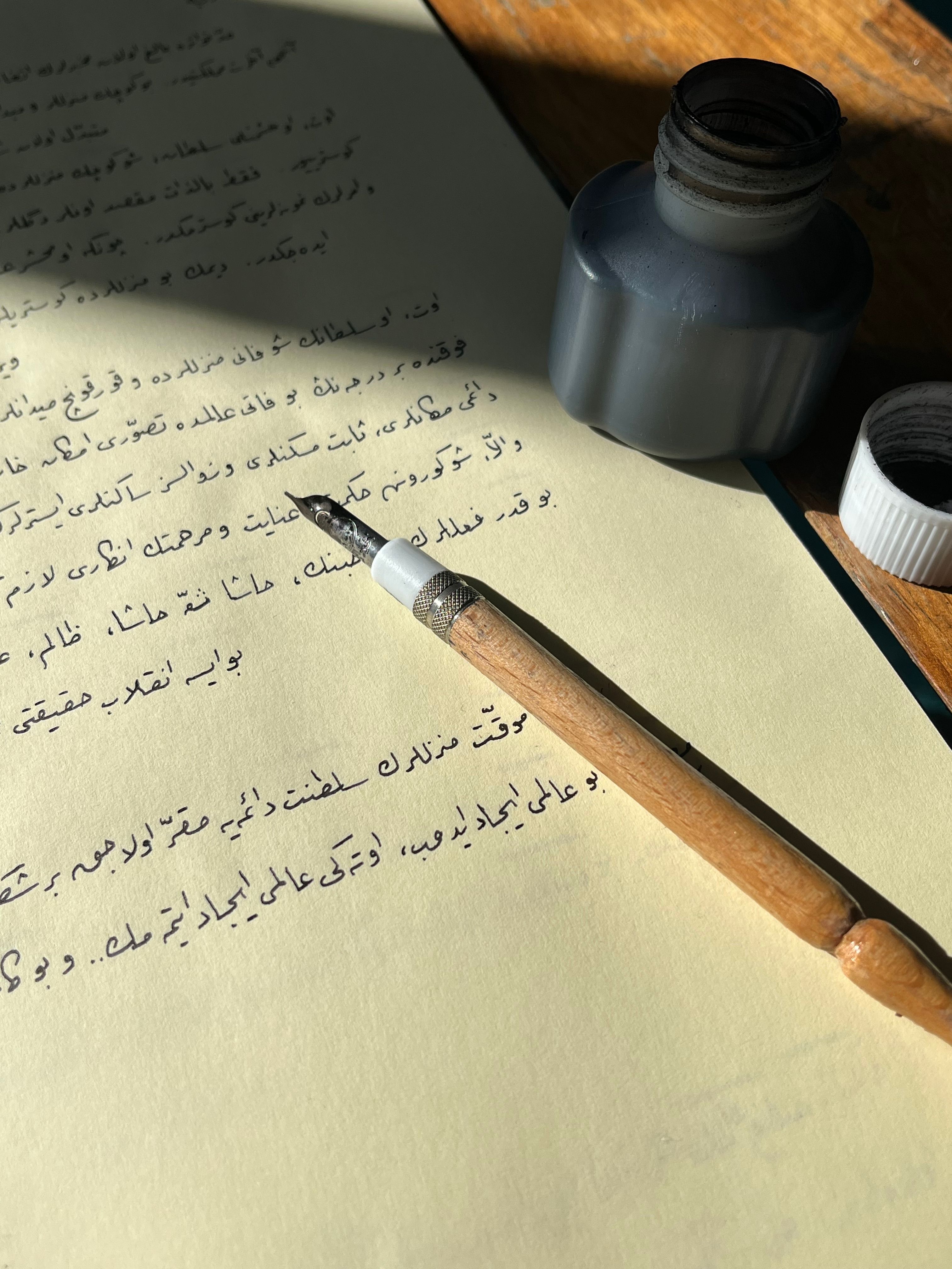 A vintage calligraphy pen rests on Arabic script paper beside an ink bottle.
