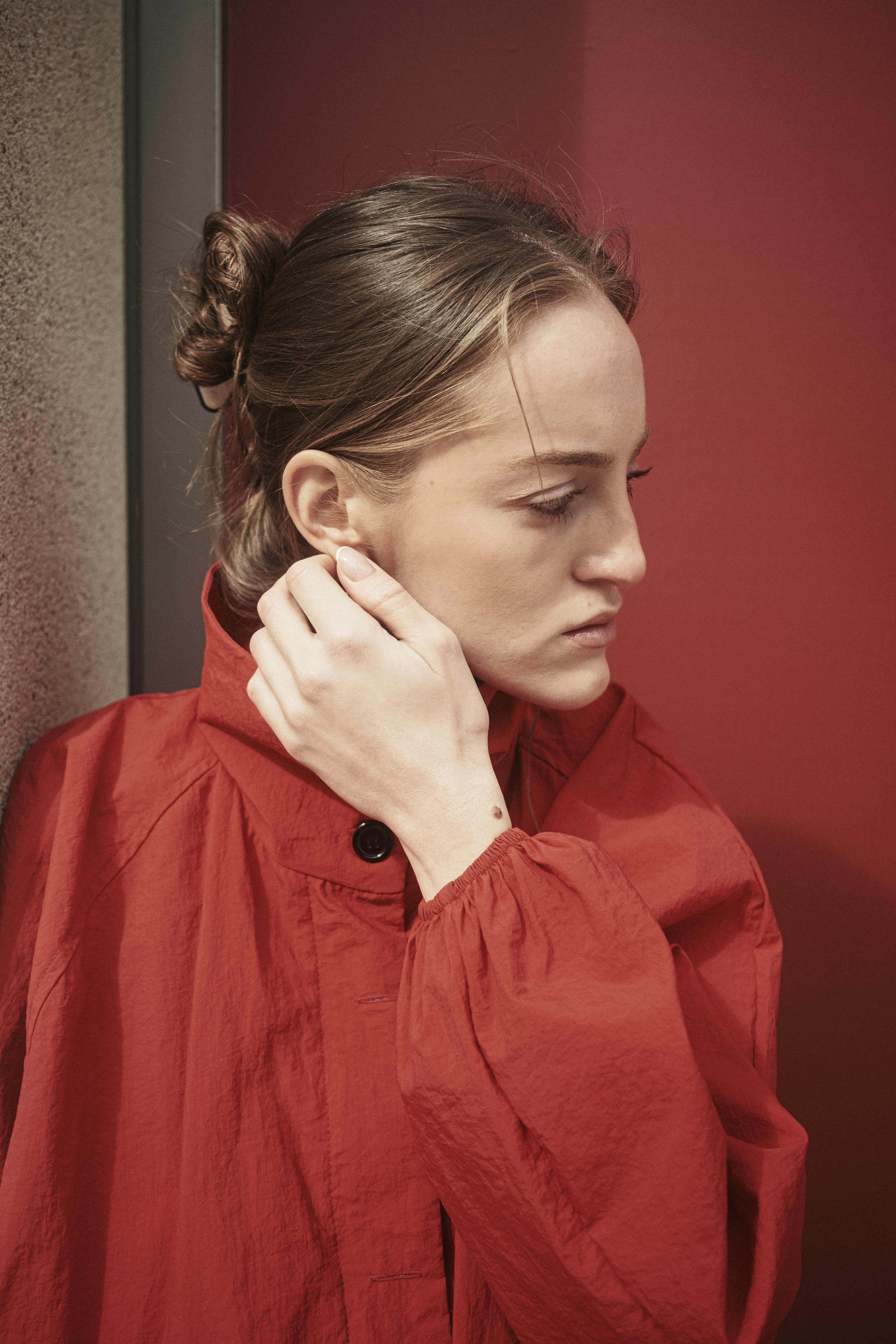 Free A profile shot of a woman in a red coat, standing against a red and grey wall in natural light. Stock Photo