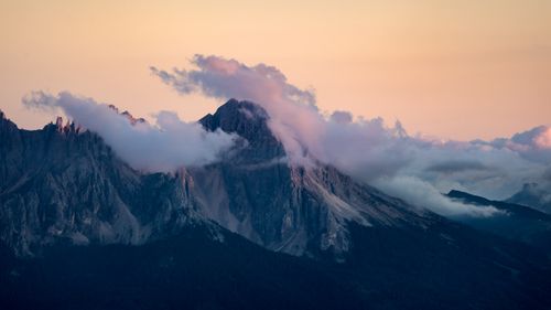 Free Breathtaking view of the Dolomites as clouds embrace the peaks during a vibrant sunset. Stock Photo