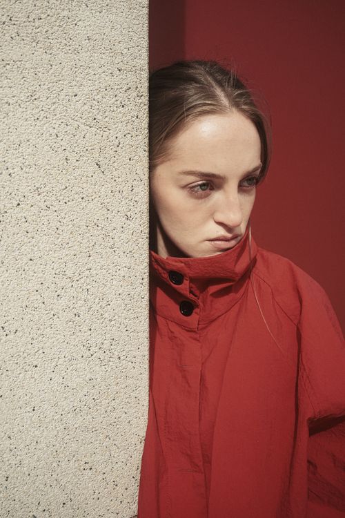 Free A woman in a red coat leans against a textured wall, lost in thought. Stock Photo