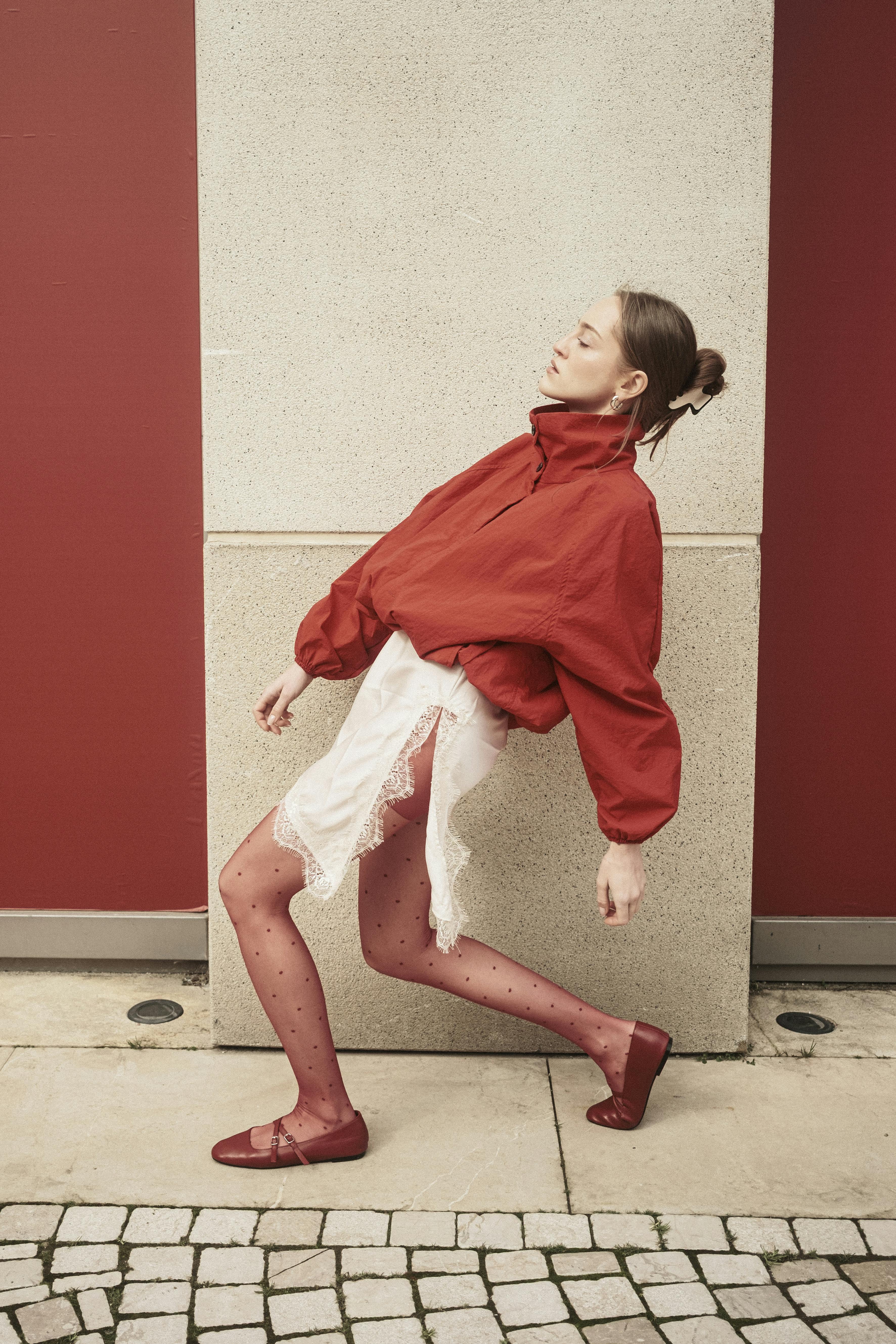 A stylish woman in red attire poses creatively against a textured wall, showcasing fashion in İstanbul, Turkey.