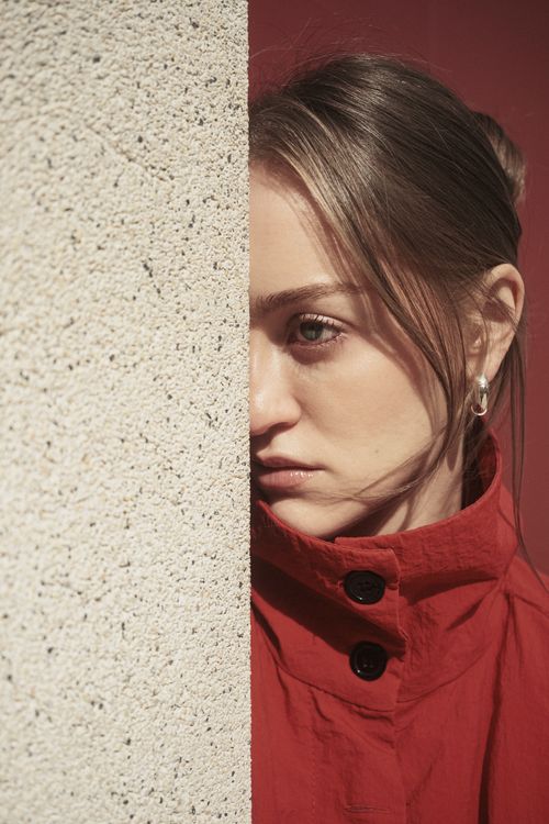 Free Half of the woman's face in red coat is visible as she leans against a wall, deep in thought. Stock Photo