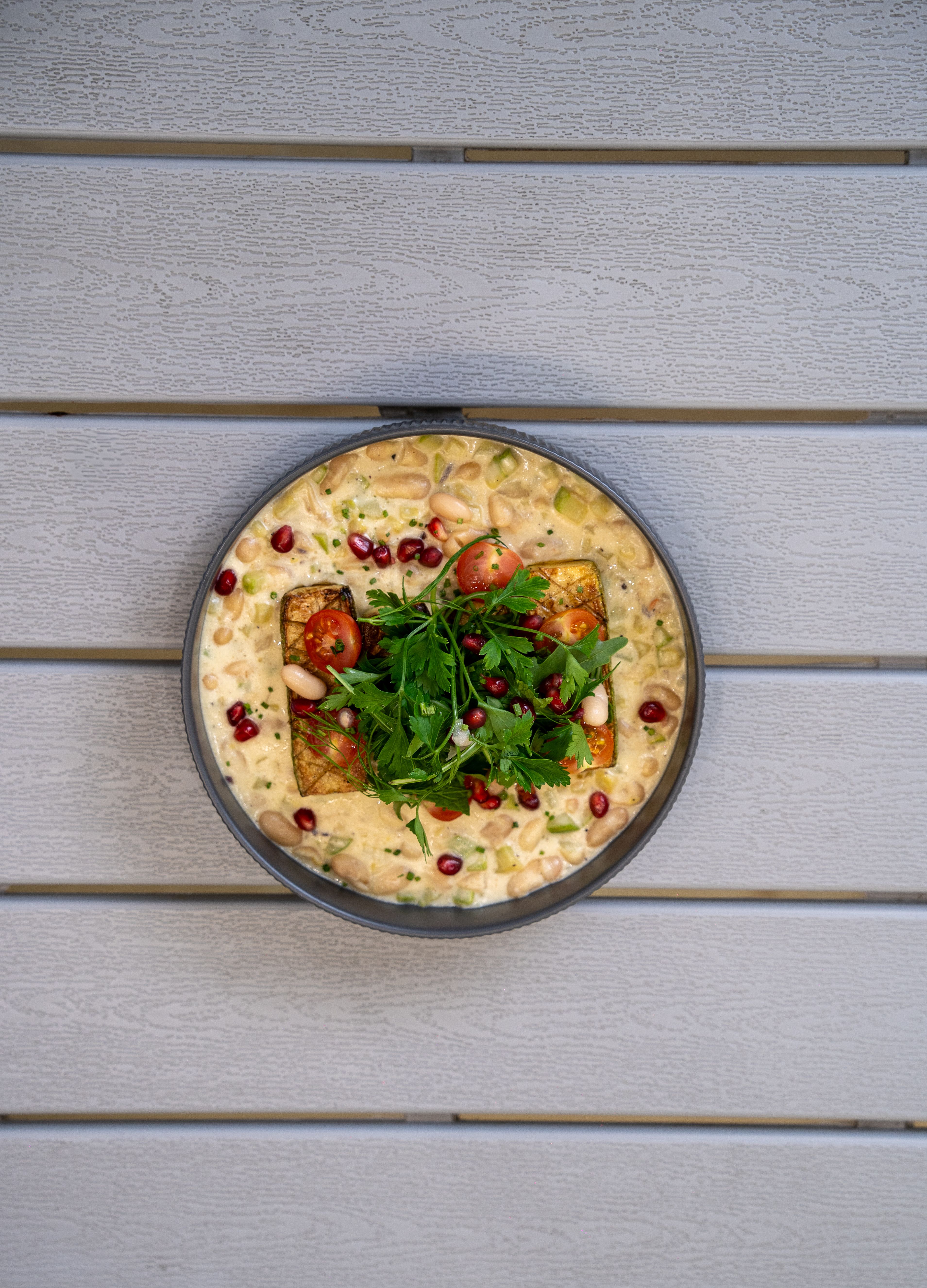 Overhead view of a fresh vegan salad with pomegranate seeds and greens, served on a wooden surface.