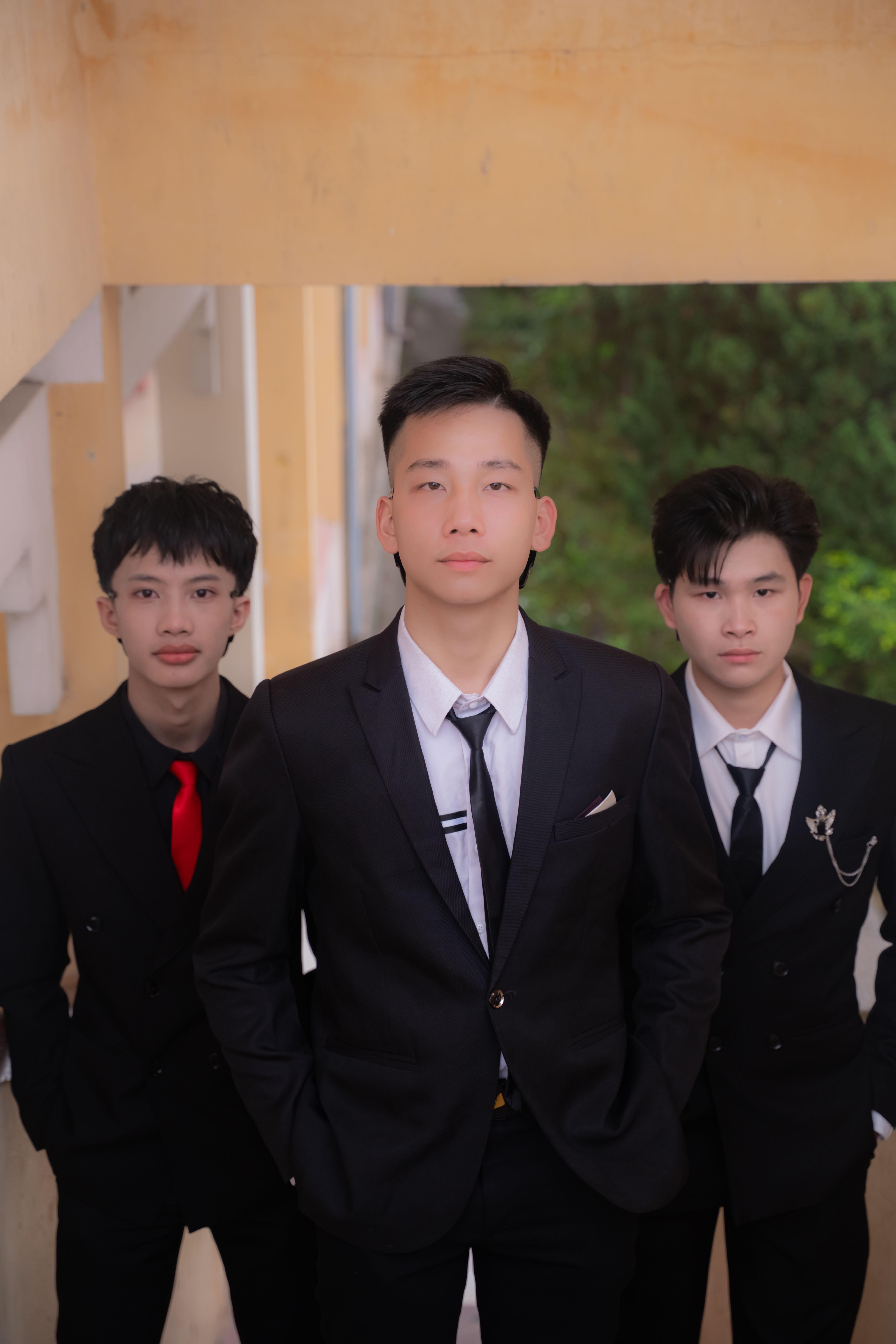 Three young men in formal black suits pose confidently, exuding style and sophistication.