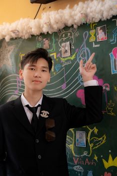 Smartly dressed young adult pointing at a creative, colorful chalkboard indoors.