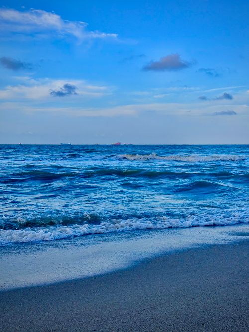 Free Peaceful ocean waves gently lap a sandy beach under a blue sky. Stock Photo