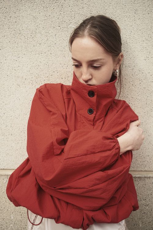 Free Stylish young woman in a bold red jacket posing thoughtfully against a textured wall. Stock Photo