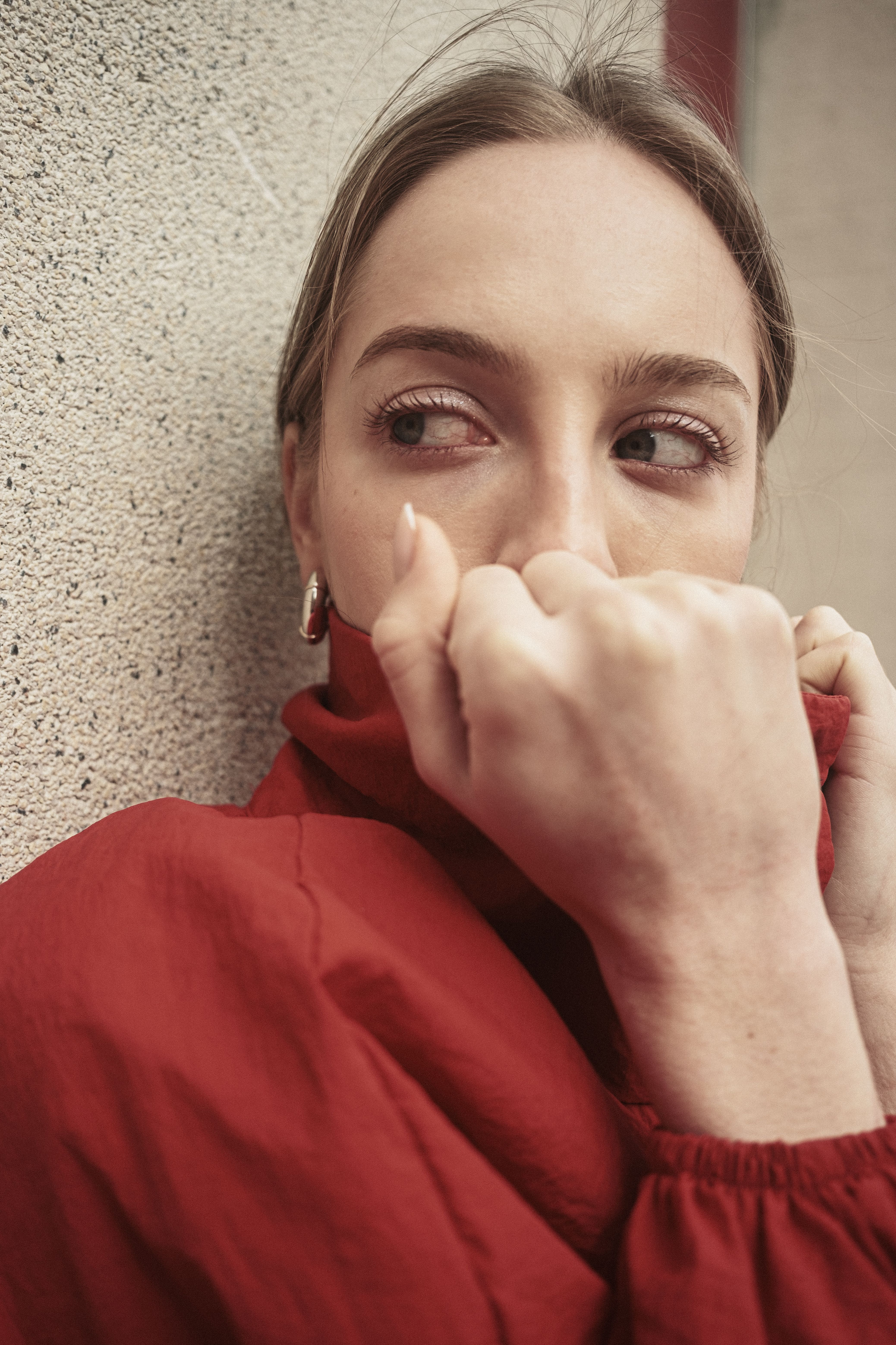 Close-up of a woman in a red jacket looking sideways against a wall, captured outdoors in İstanbul.