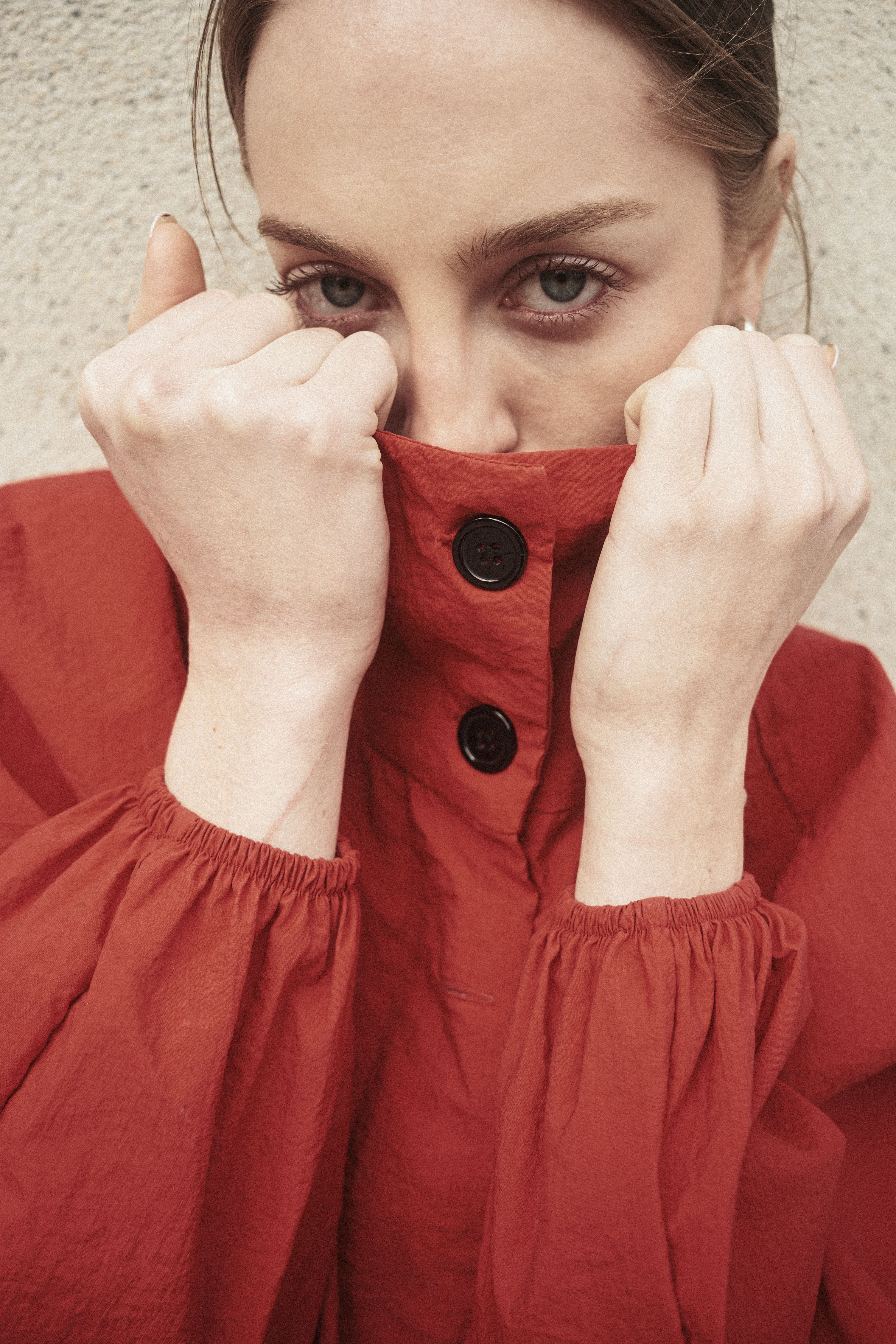 Close-up portrait of woman hiding face with red coat, featuring black button details.