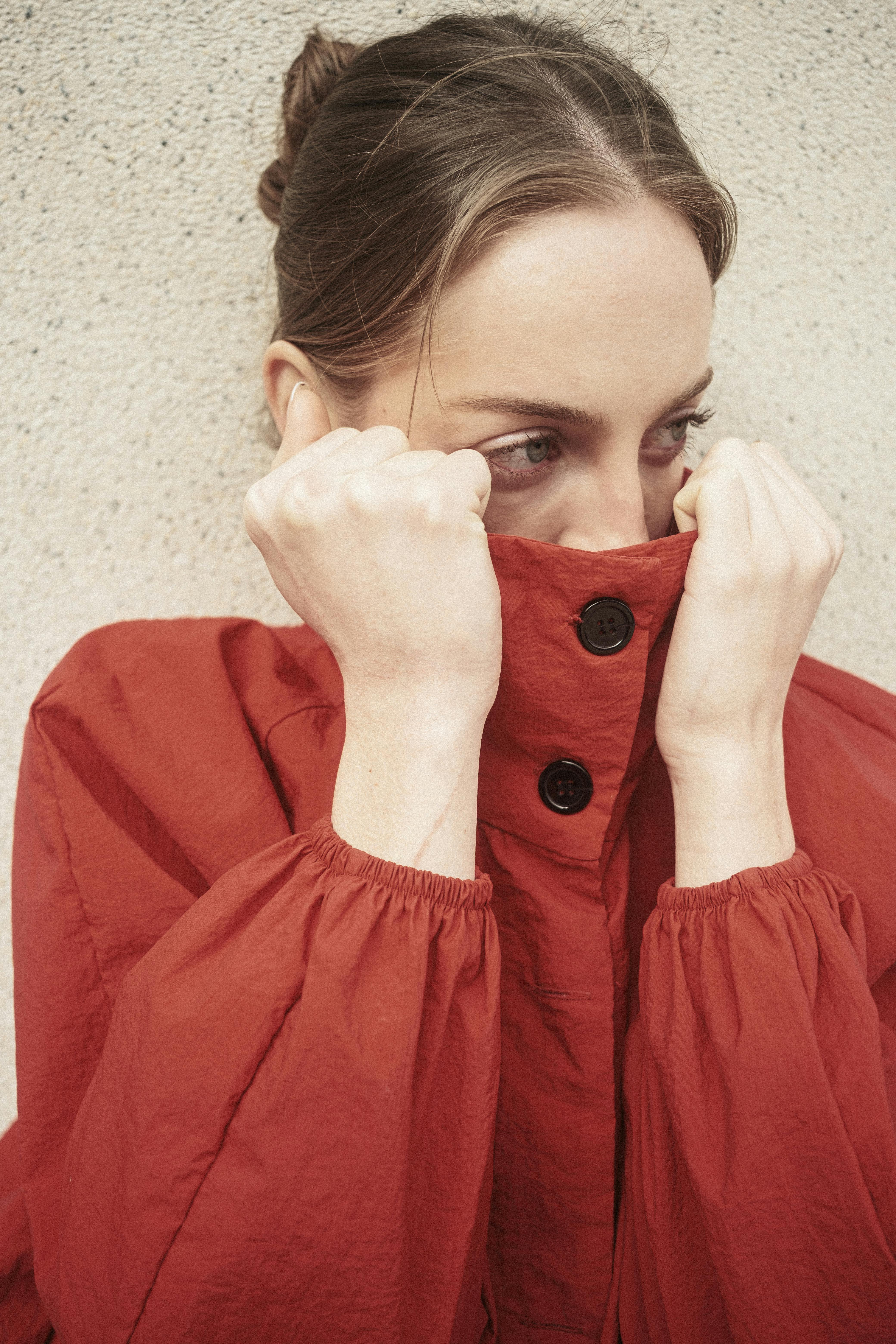 Portrait of a woman partially hiding her face with a red coat, outdoors.