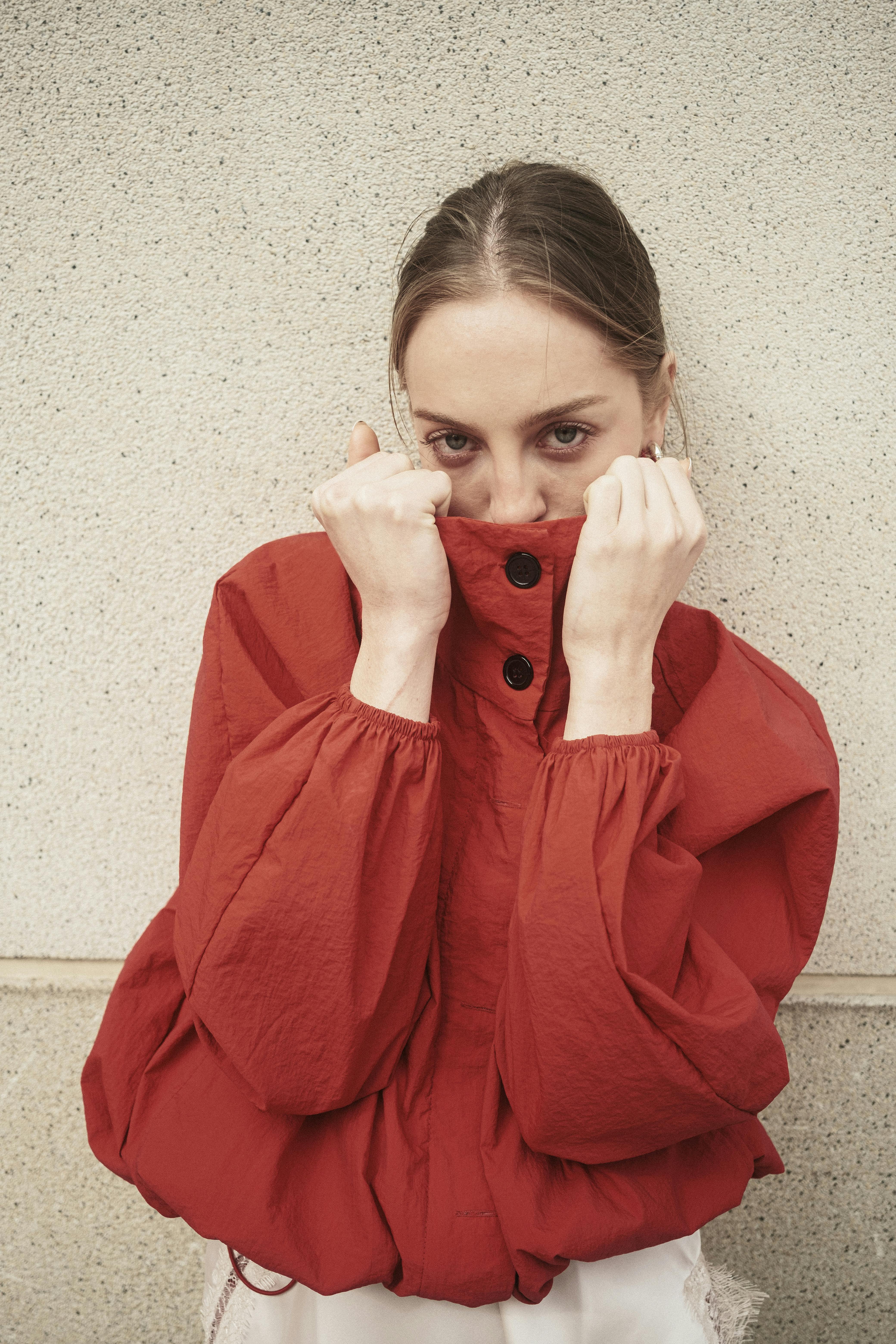 Young woman in a red jacket poses confidently against a neutral wall.