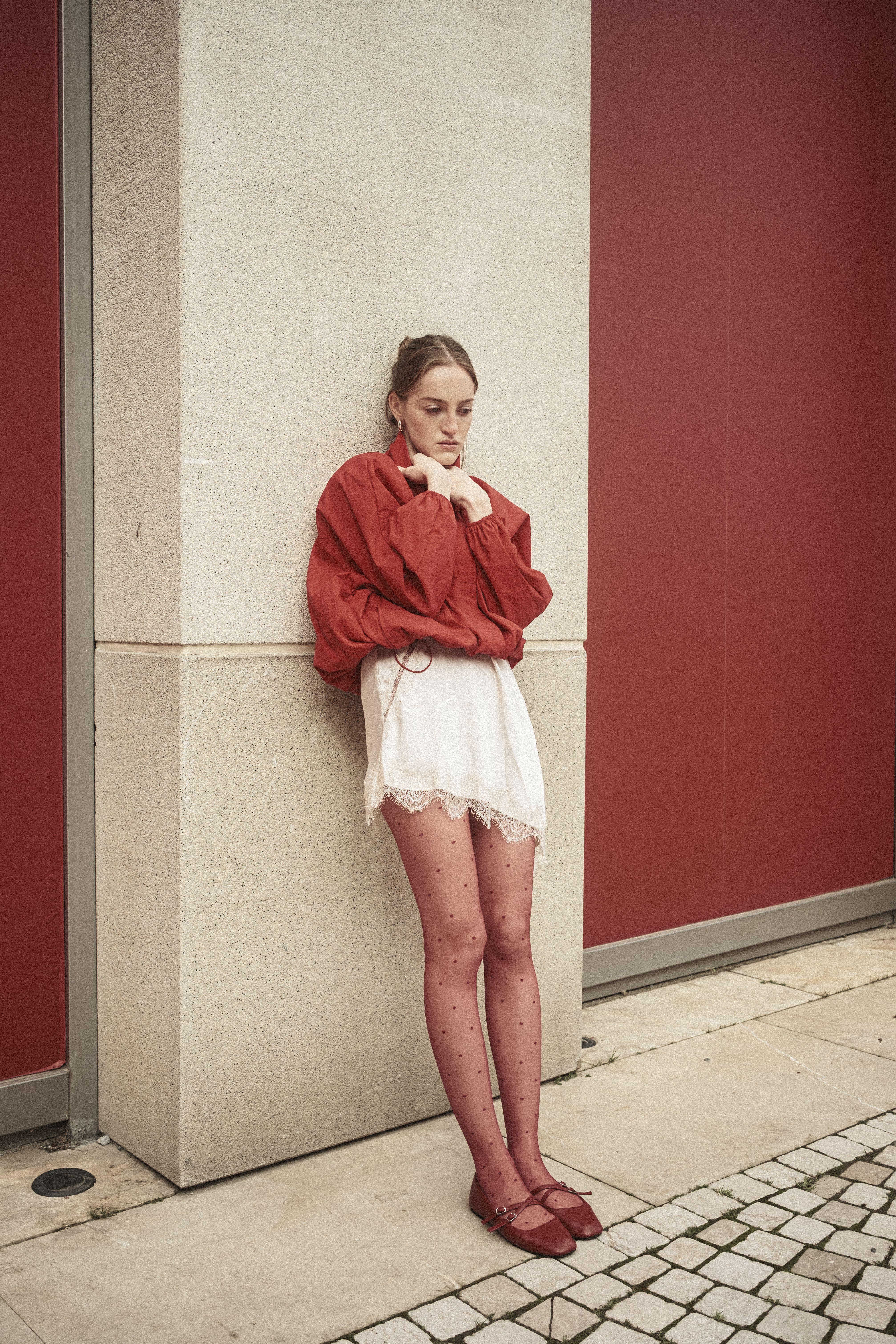 Stylish young woman in red and white outfit leaning on a wall in Istanbul.