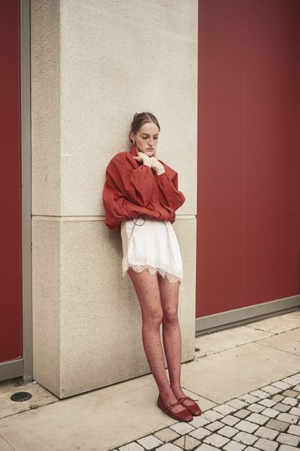 Stylish young woman in red and white outfit leaning on a wall in Istanbul.